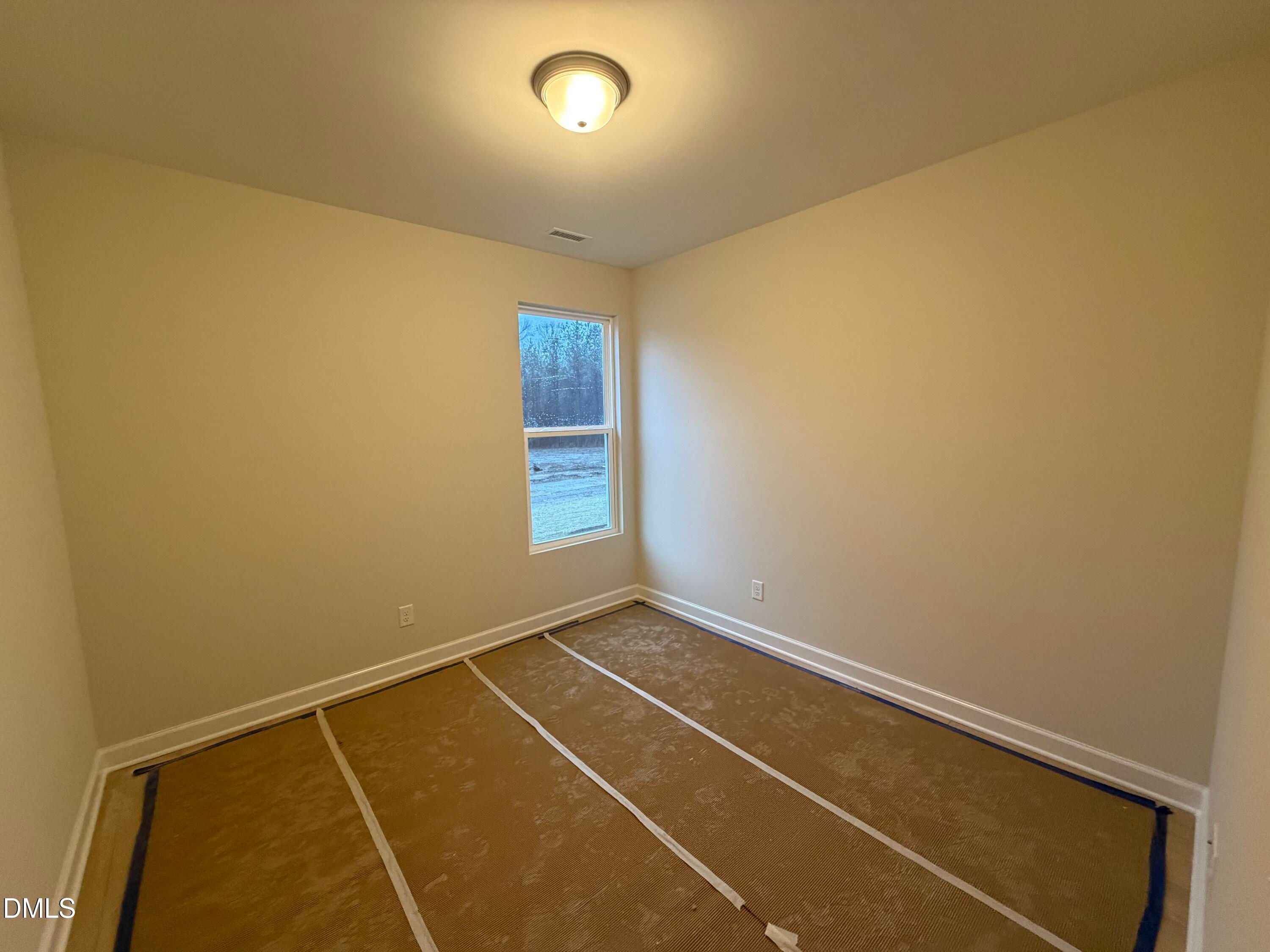 Spacious empty bedroom with beige walls, large window, and protected flooring in Davidson Homes The Daphne C, Lillington, NC