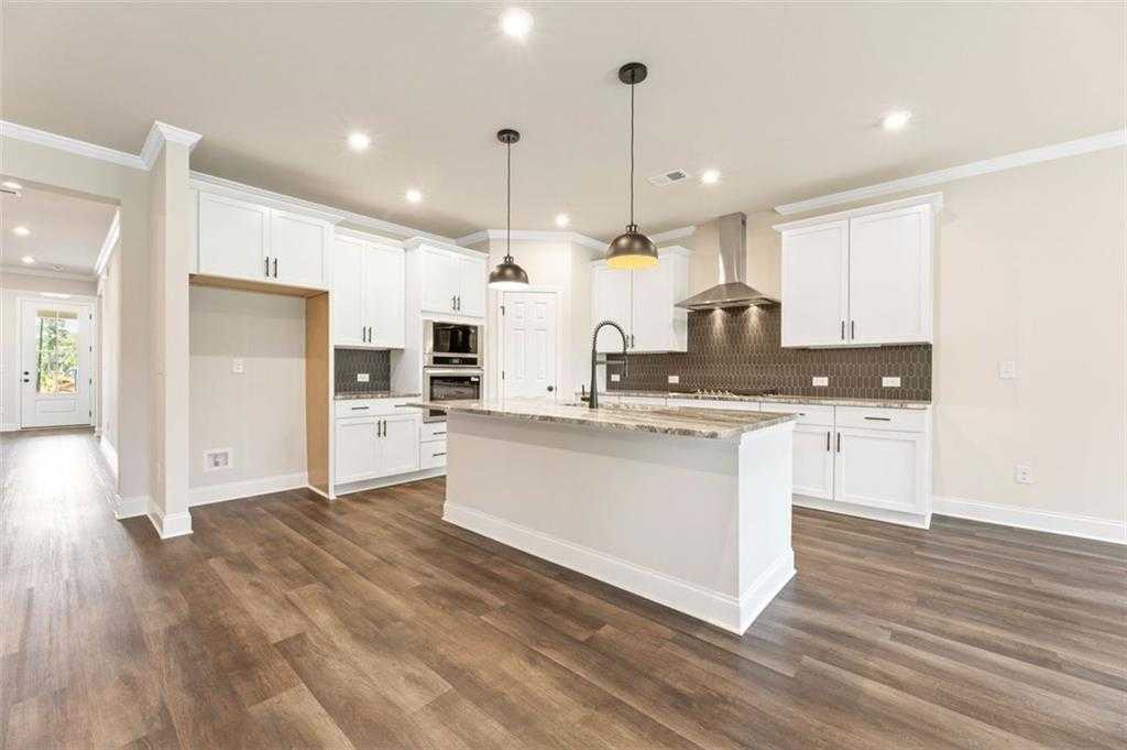 Modern white kitchen with large granite island, stainless appliances, pendant lights in Davidson Homes Harrison G, Hoschton GA