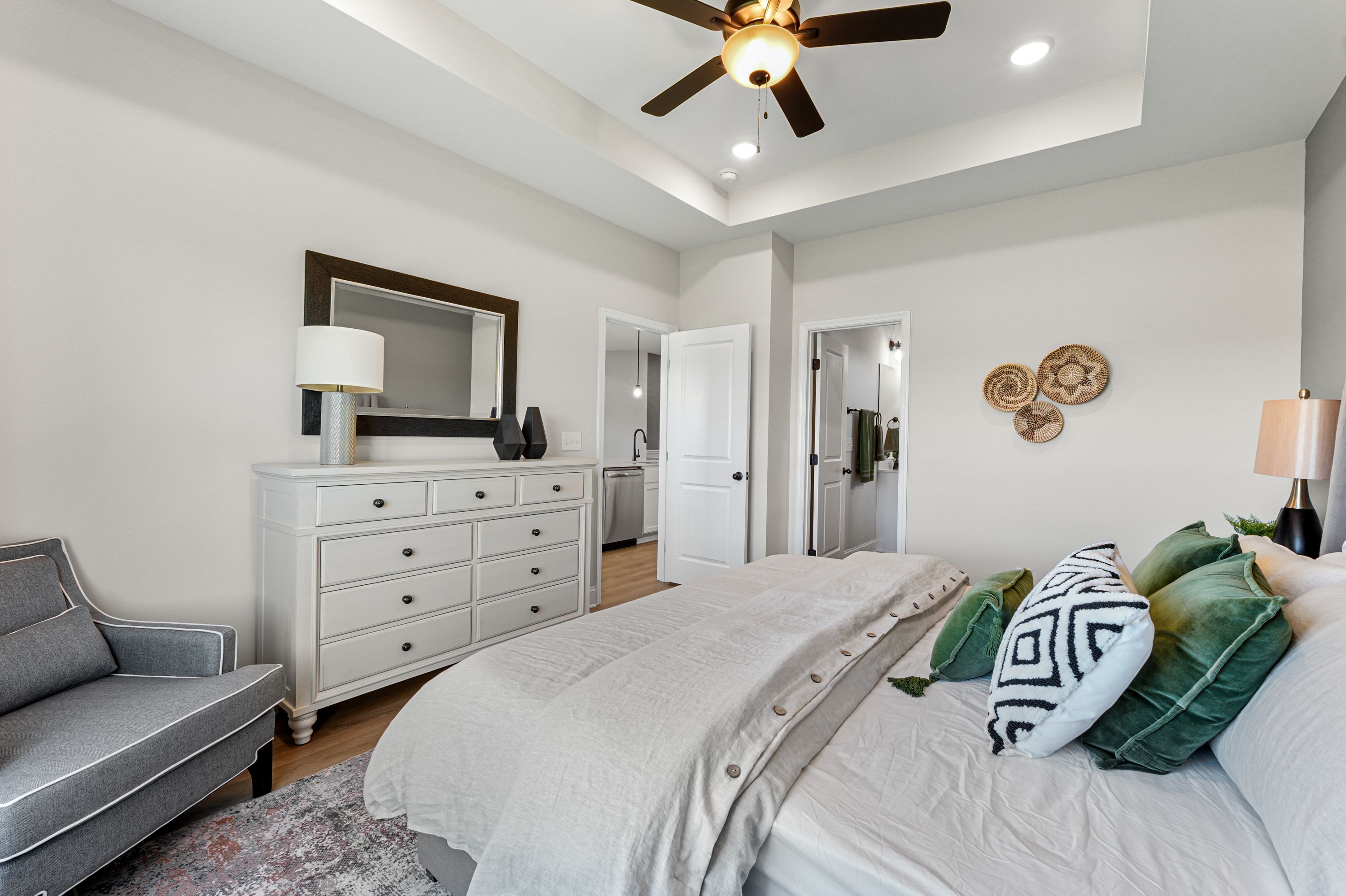 Spacious primary bedroom at Ramsay Cove in Owens Cross Roads AL with king bed, green pillows, white dresser, armchair, and en-suite bath