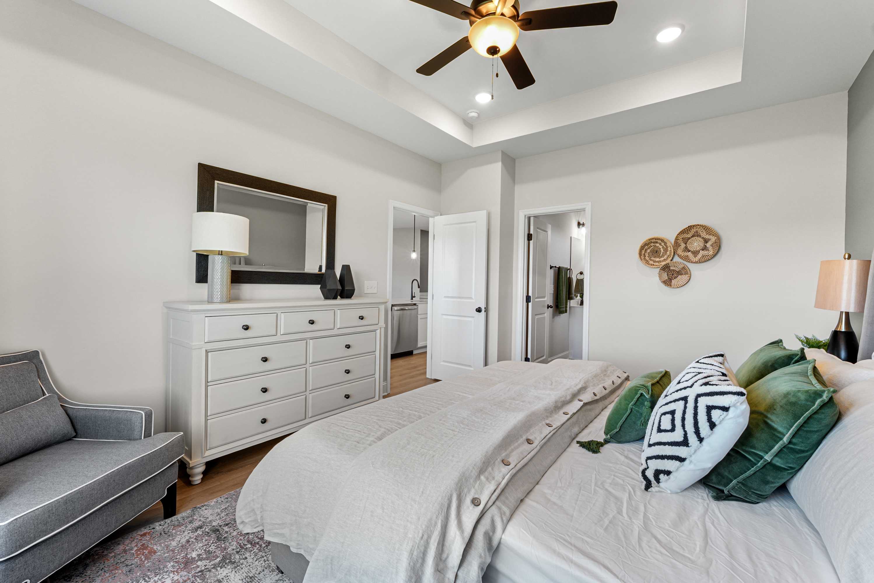 Spacious primary bedroom at Ramsay Cove in Owens Cross Roads AL with king bed, green pillows, white dresser, armchair, and en-suite bath