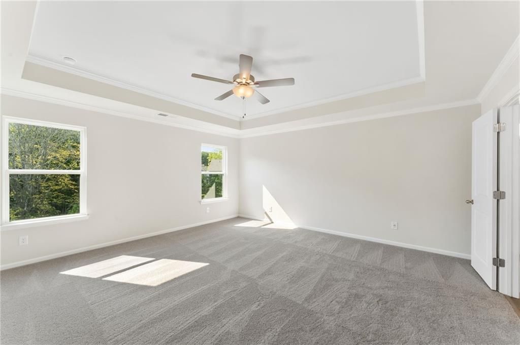 Bright bedroom with tray ceiling, ceiling fan, large windows overlooking trees, and gray carpet in Davidson Homes The Willow B, Dallas, Georgia