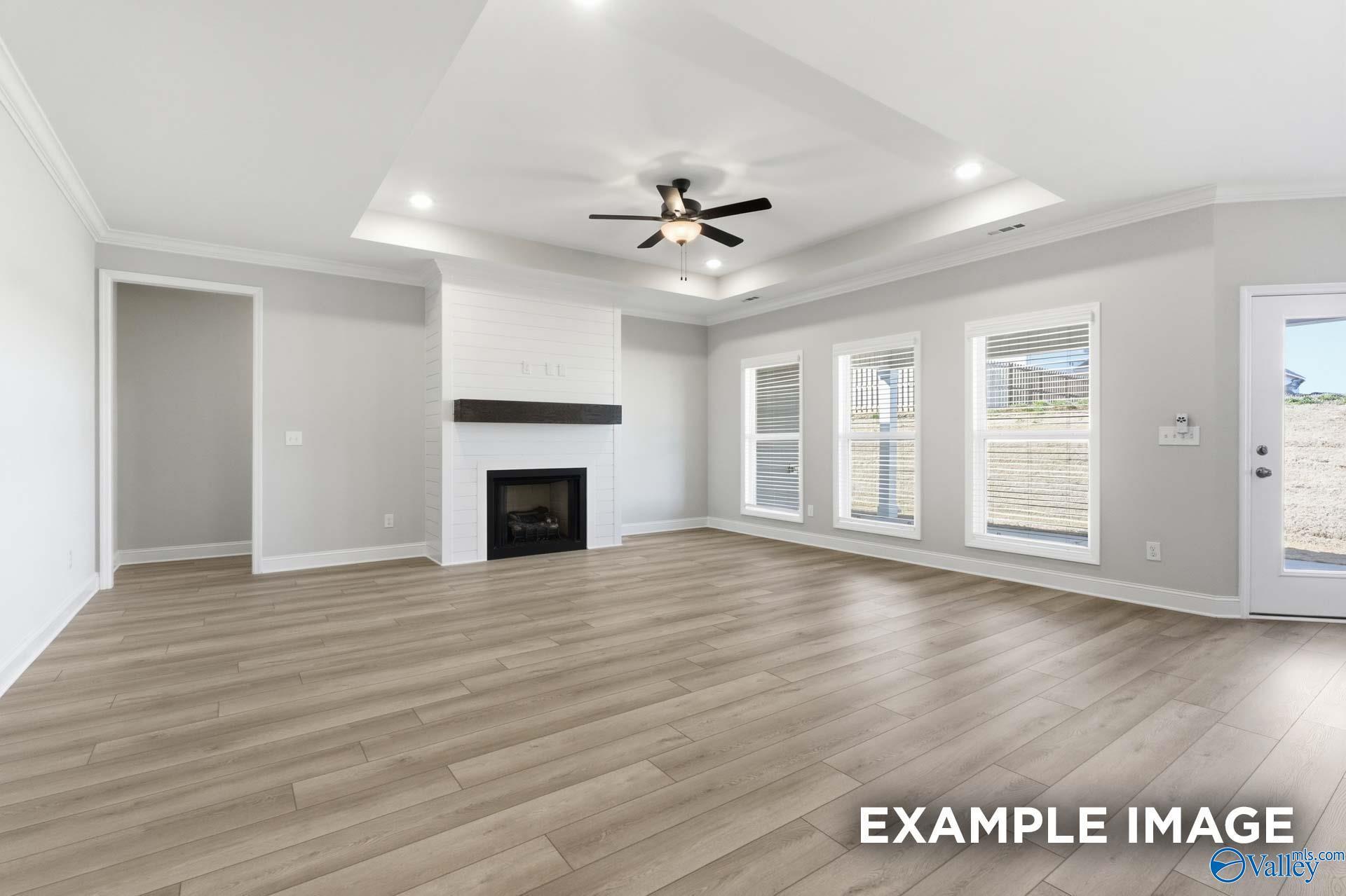 Spacious living room with white brick gas fireplace, ceiling fan, large windows, and hardwood floors in Davidson Homes The Harrison C, Madison Alabama