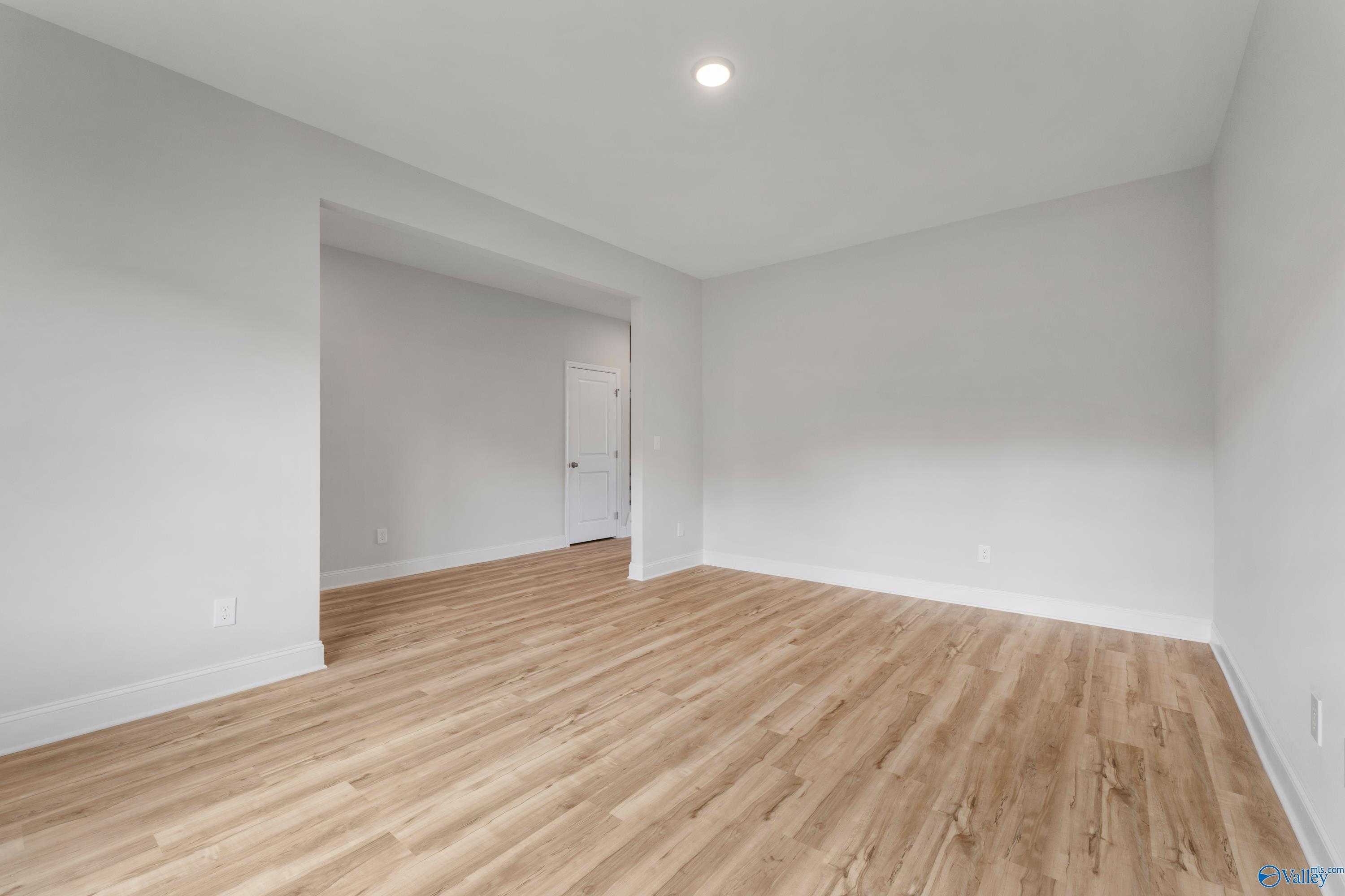 Spacious empty living room with light gray walls, hardwood floors, and archway in Davidson Homes Chelsea C, Harvest Alabama