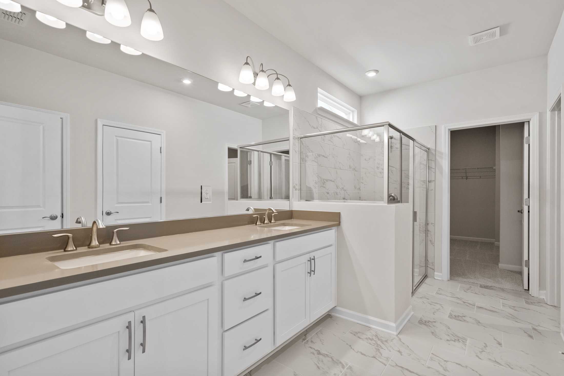 Modern master bathroom in The Dawson featuring double vanity, large mirror, and frameless glass shower