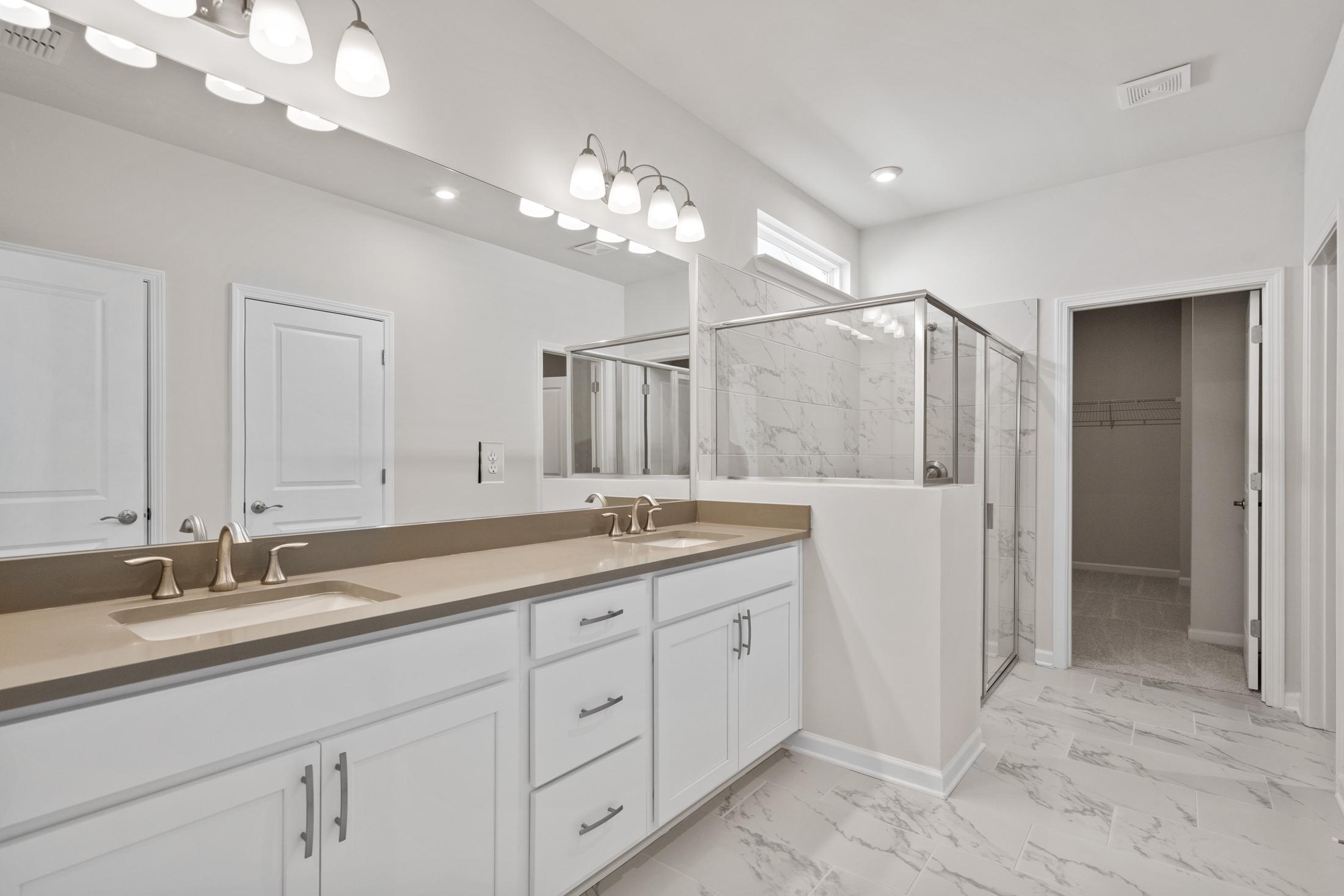 Modern master bathroom in The Dawson featuring double vanity, large mirror, and frameless glass shower