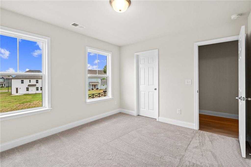 Bright secondary bedroom with beige carpet, large windows overlooking green yard and homes in Davidson Homes The Hickory B at Wehunt Meadows, Hoschton, Georgia