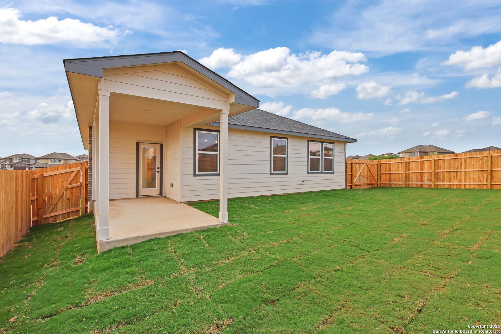 Covered back patio with sliding glass doors on beige single-story home, fenced lush green yard in Comanche Ridge, San Antonio