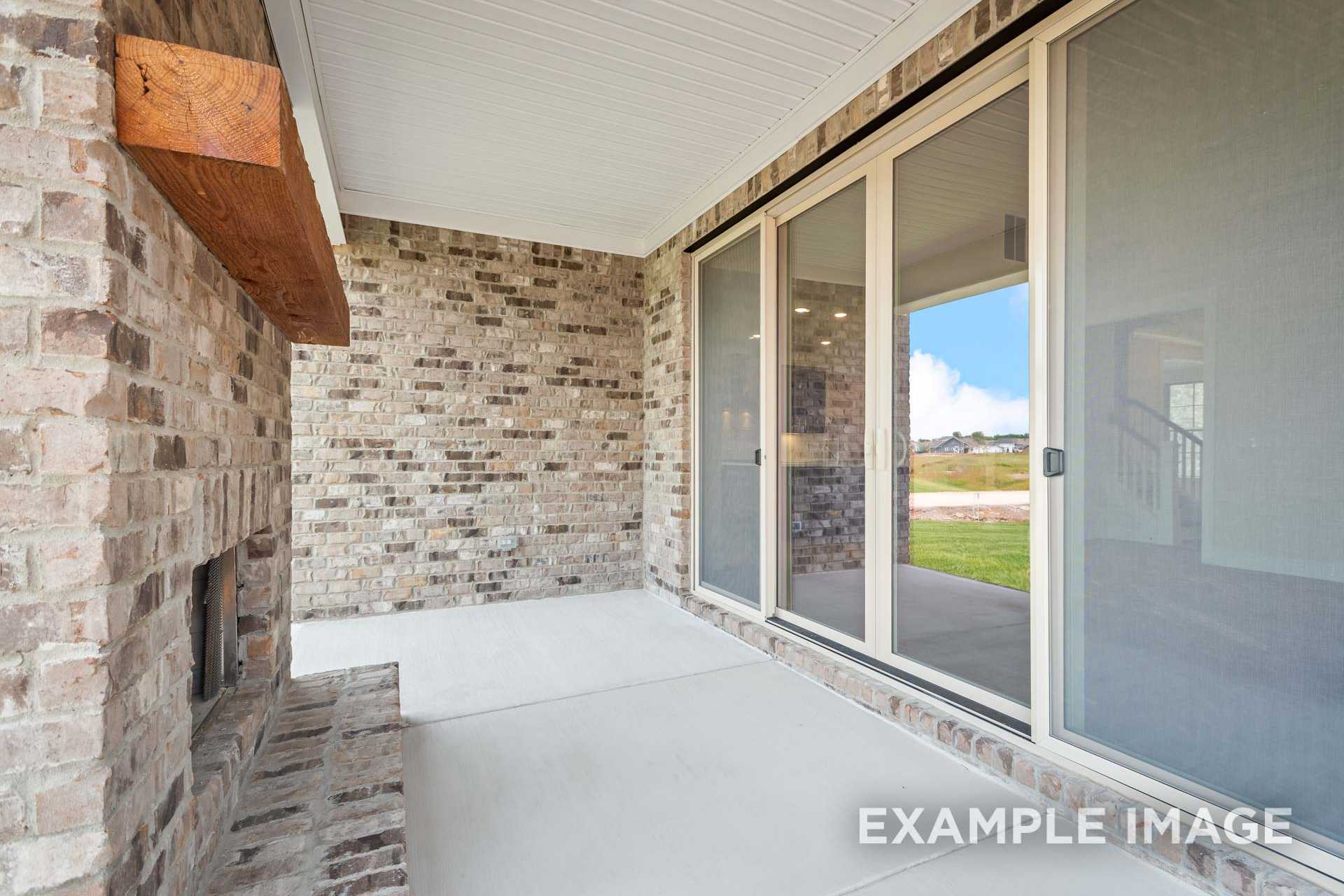 Covered patio in The Hawkins Davidson Homes design with brick fireplace, wooden mantel, and sliding glass doors to lawn