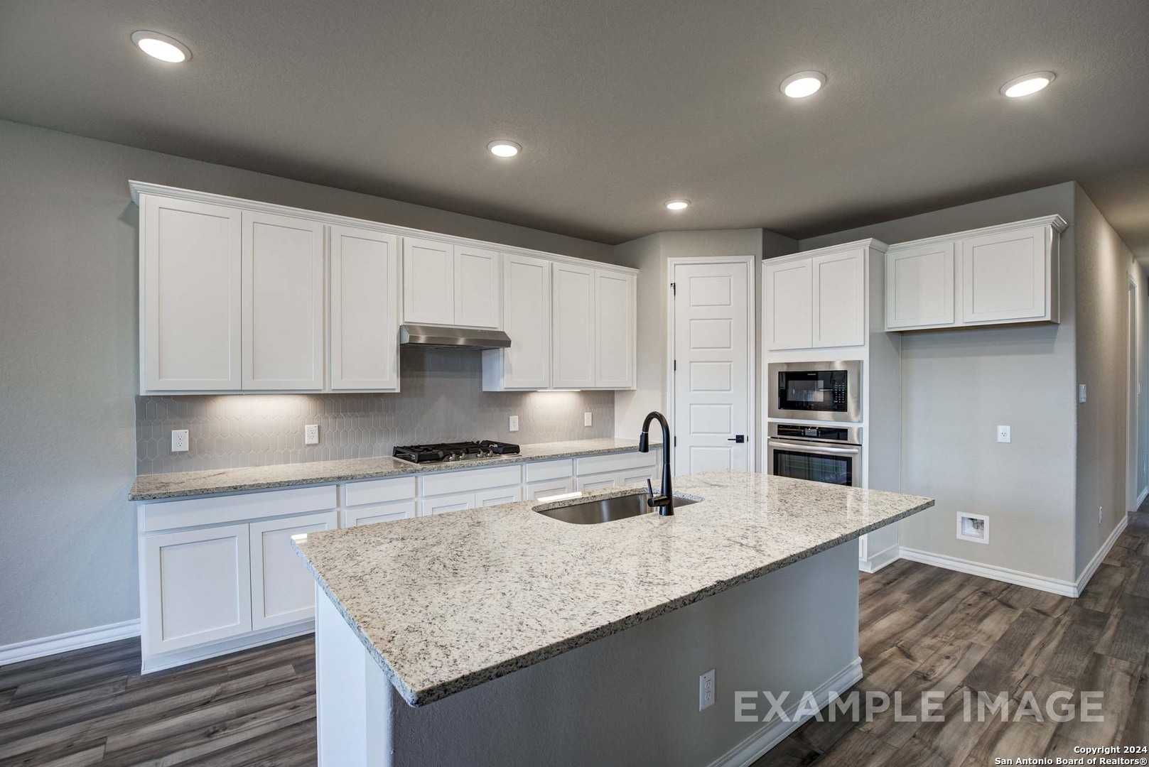Modern white kitchen with granite island, stainless appliances, and open layout in Davidson Homes The Rockford G, Ladera, San Antonio