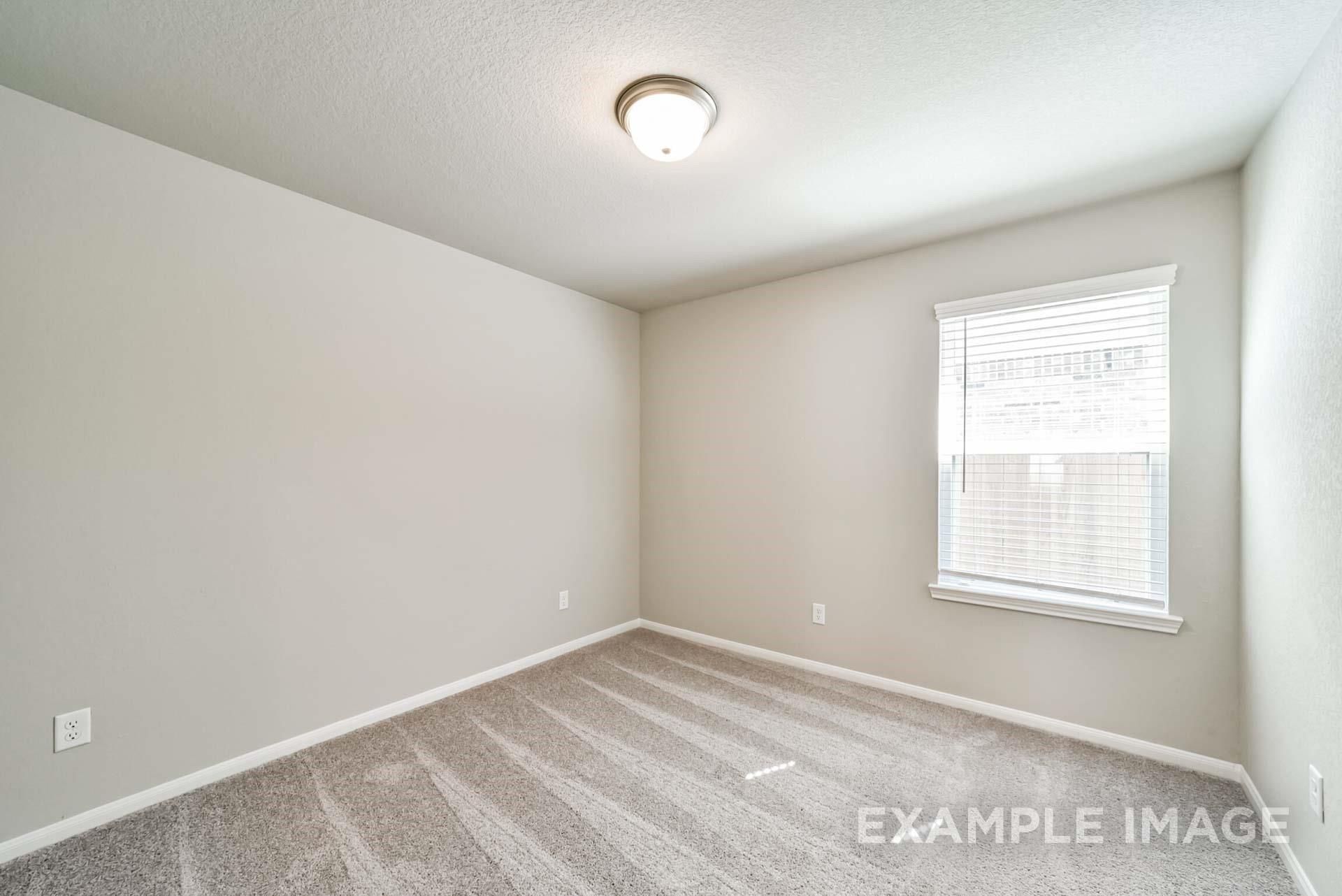 Spacious guest bedroom with neutral walls and plush carpeting in The Riviera A floor plan at Emberly in Beasley, Texas.