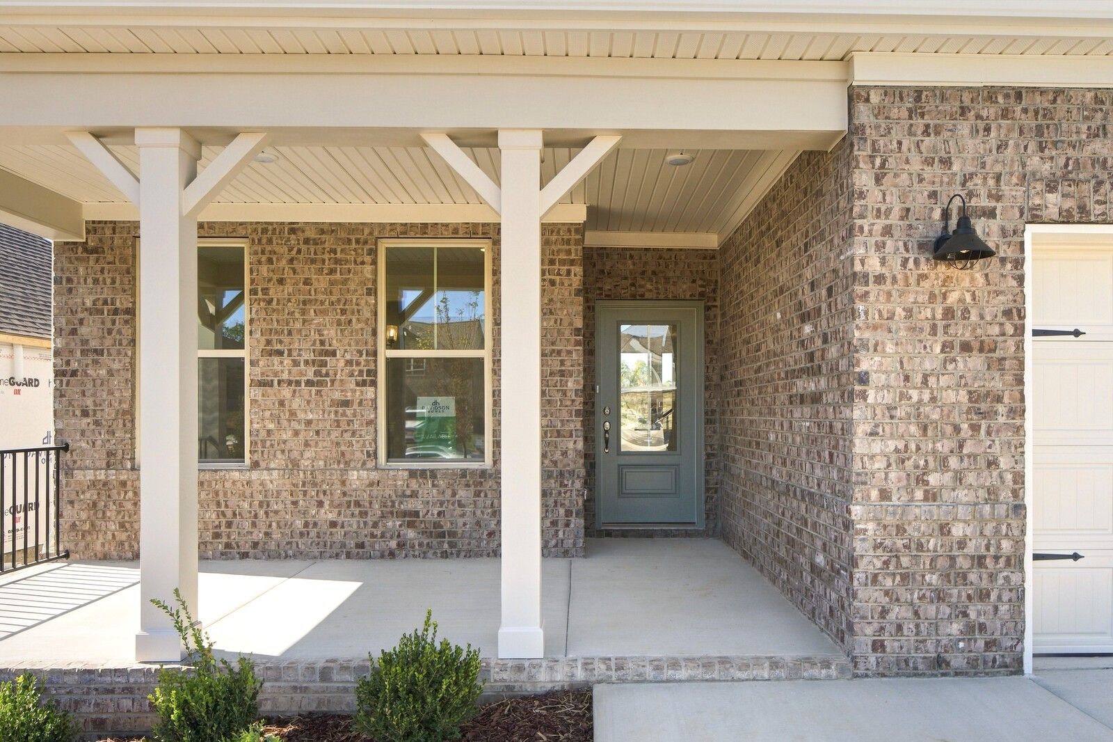 Brick front porch with white columns and sage green door at Davidson Homes' The Willow B in Woods Crossing, Gallatin, TN