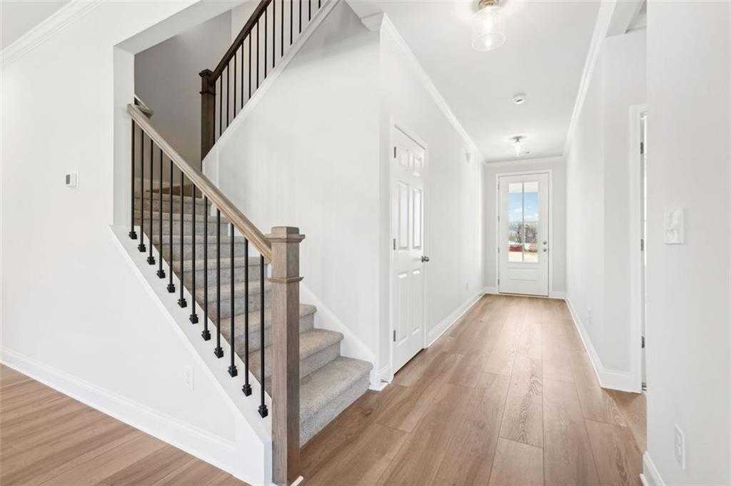 Bright hallway with wooden staircase, black metal balusters, and hardwood floors in Davidson Homes Hickory C, Hoschton, GA