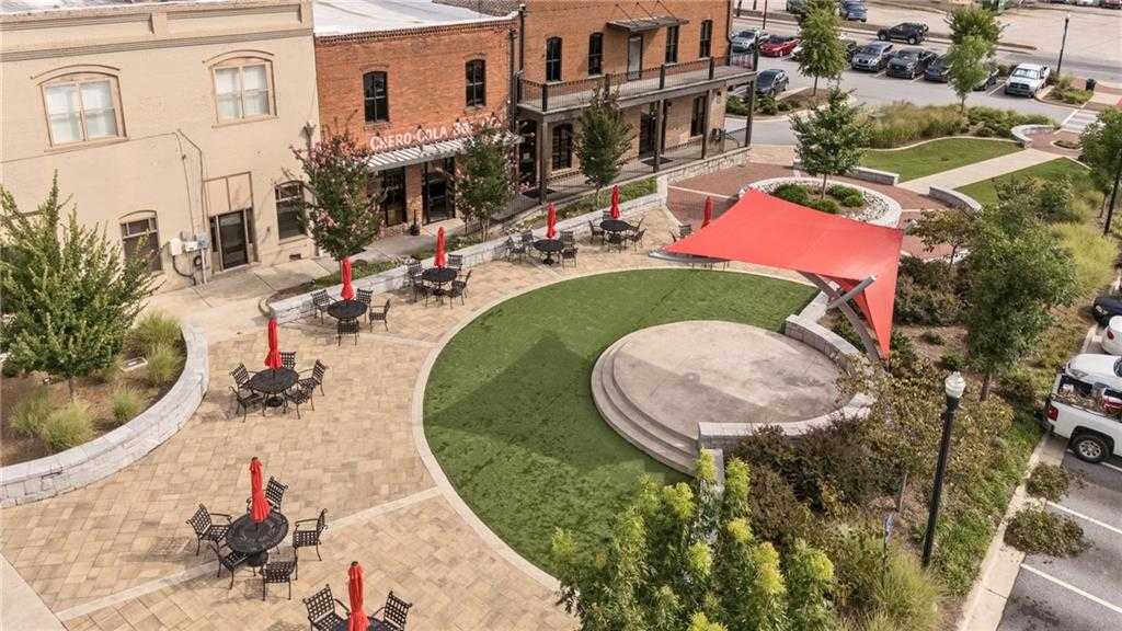 Vibrant Cedar Farms courtyard in Winder, Georgia, featuring red umbrellas, bistro tables on pavers, circular stage, brick buildings, and lush greenery