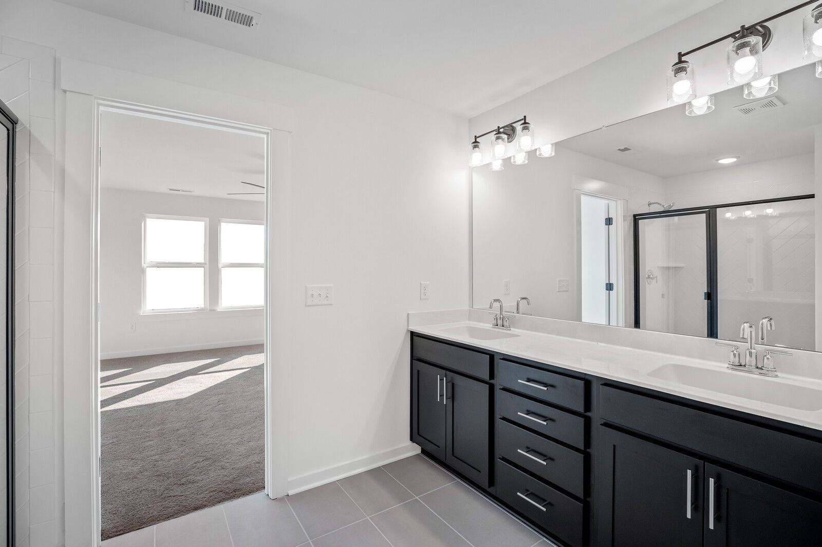 Modern master bathroom with double vanity, black cabinets, glass shower, and bedroom view in Davidson Homes Willow C, Gallatin, TN