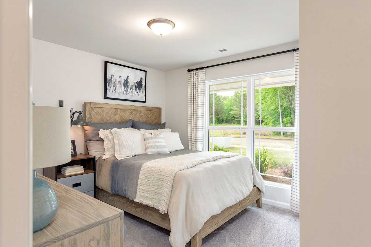 Spacious master bedroom in The Franklin home with rustic wooden headboard, plush gray bedding, and large window view
