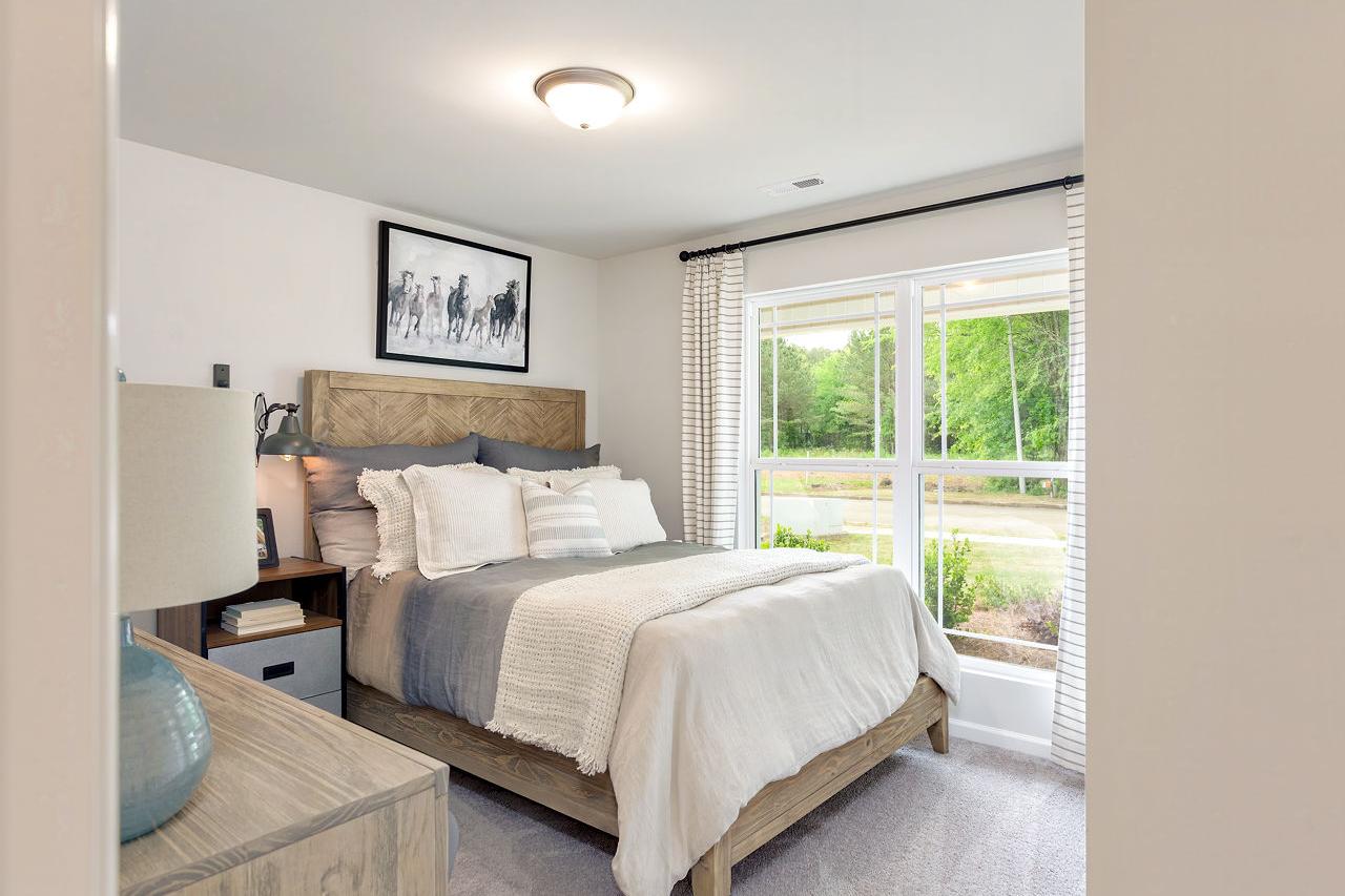 Spacious master bedroom in The Franklin home with rustic wooden headboard, plush gray bedding, and large window view