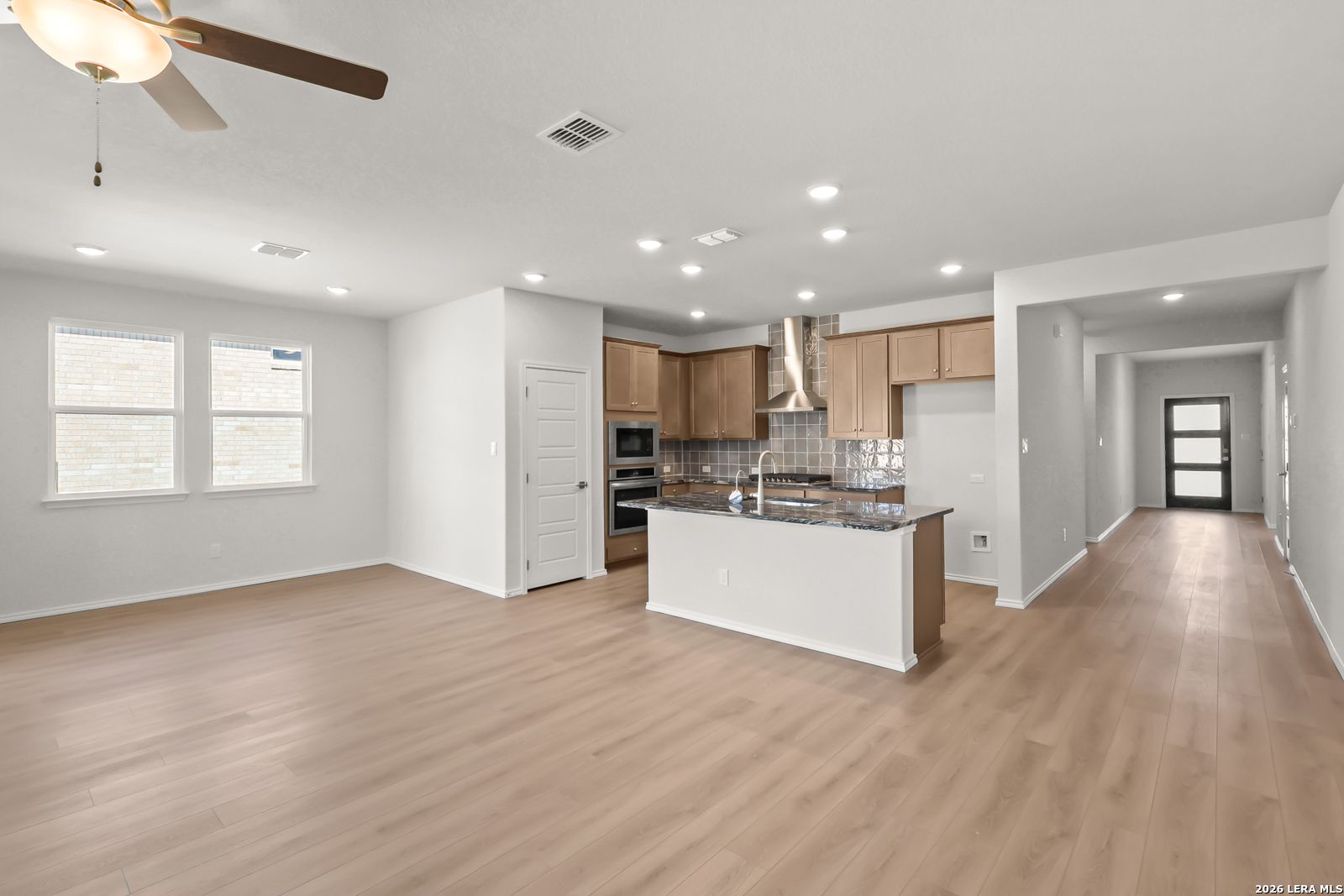 Open-concept kitchen with island, wood-tone cabinets, and luxury vinyl flooring in The Daphne I by Davidson Homes, Bricewood San Antonio