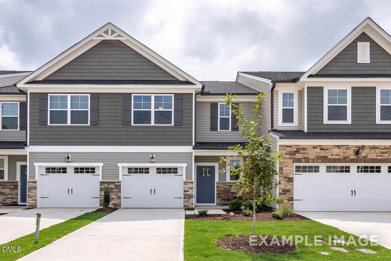 Modern two-story townhomes with gray siding, brick accents, garages, and landscaped front yard in Springvale, Fuquay-Varina, NC by Davidson Homes
