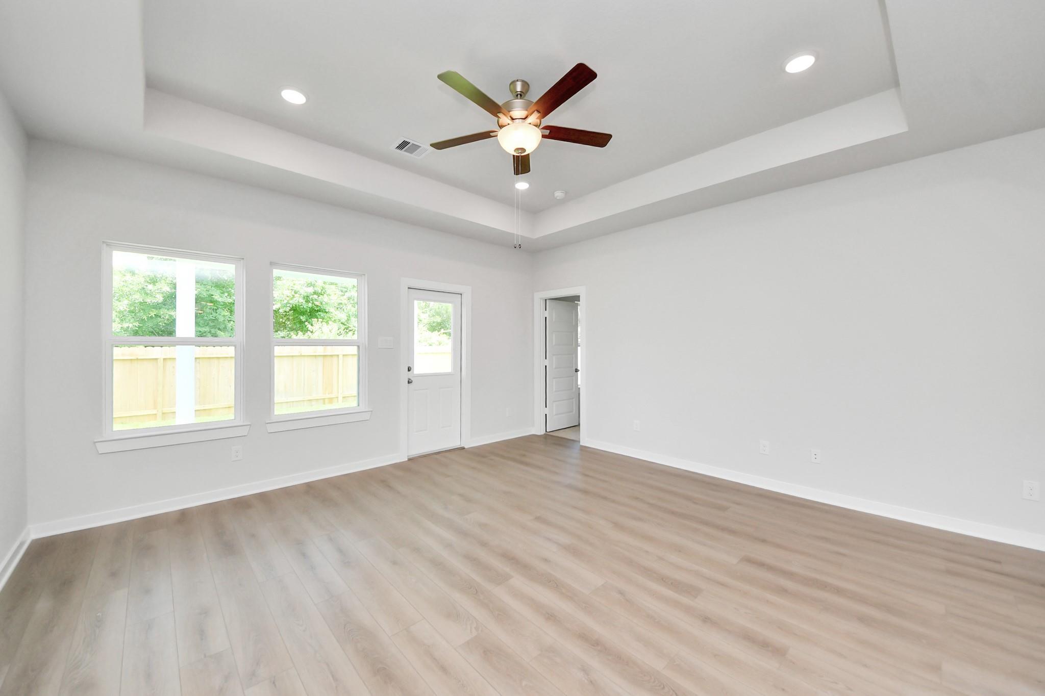 Spacious living room with tray ceiling and ceiling fan in The Blanco E floor plan at Caney Creek Place, Conroe, Texas.
