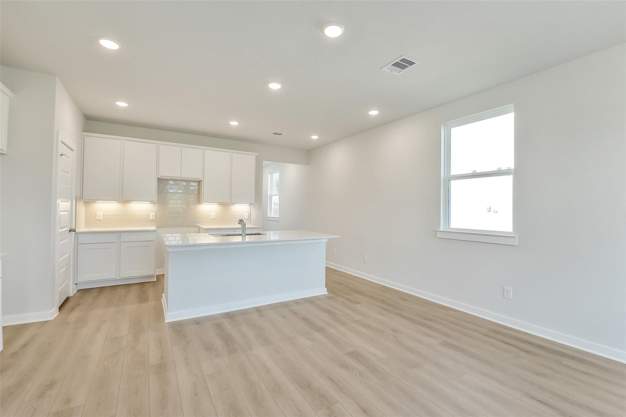 Modern white kitchen with spacious island sink, recessed lights, and hardwood floors in Davidson Homes The Colorado F, Cleveland, TX
