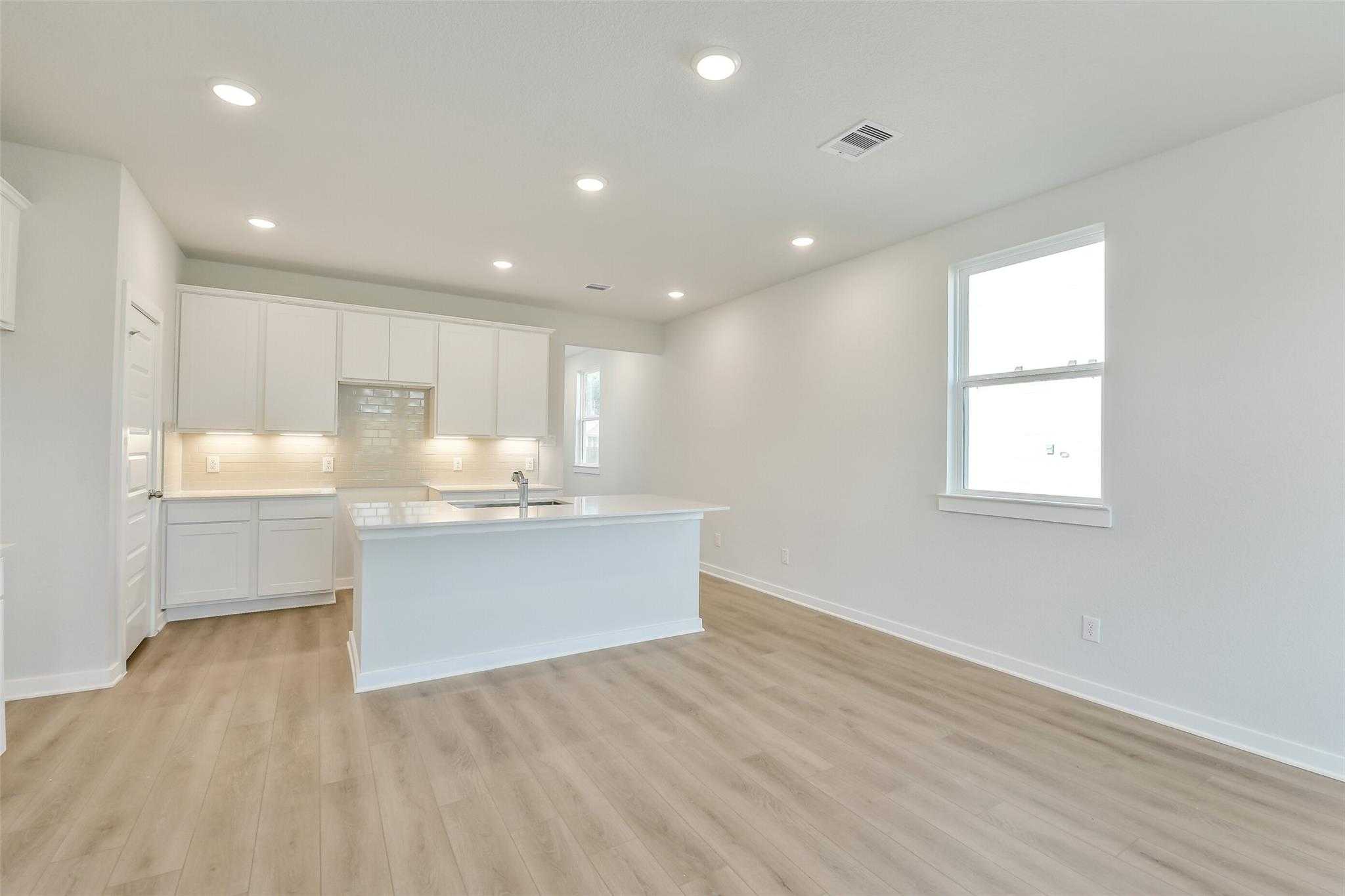 Modern white kitchen with large island sink, recessed lights, and light wood floors in Davidson Homes Colorado F, Cleveland TX