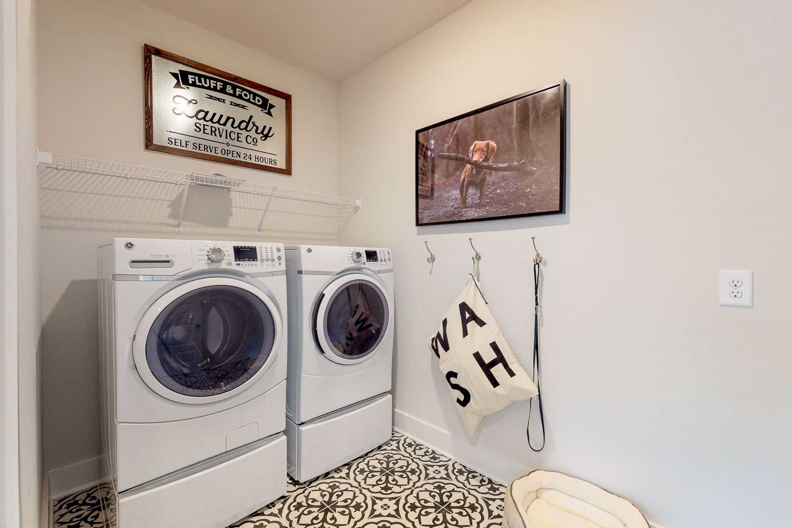 Spacious laundry room at Liberty Creek in Gallatin TN featuring white washer dryer set, vintage Fluff & Fold sign, and tiled floor