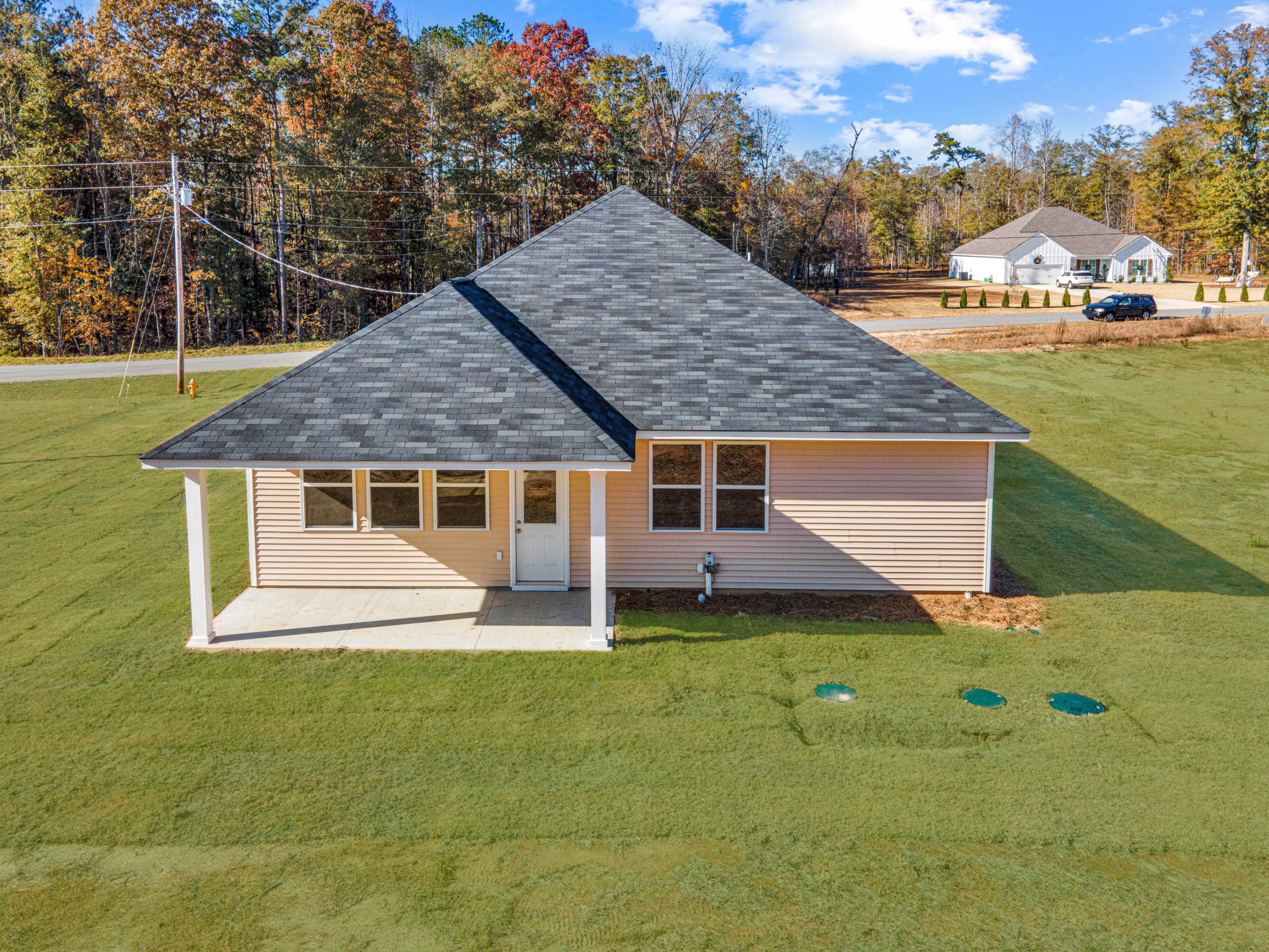 Single-story 4-bedroom home exterior with beige siding, dark roof, one-car garage amid pine trees in Silver Oak, Cusseta, Alabama by Evermore Homes Orion