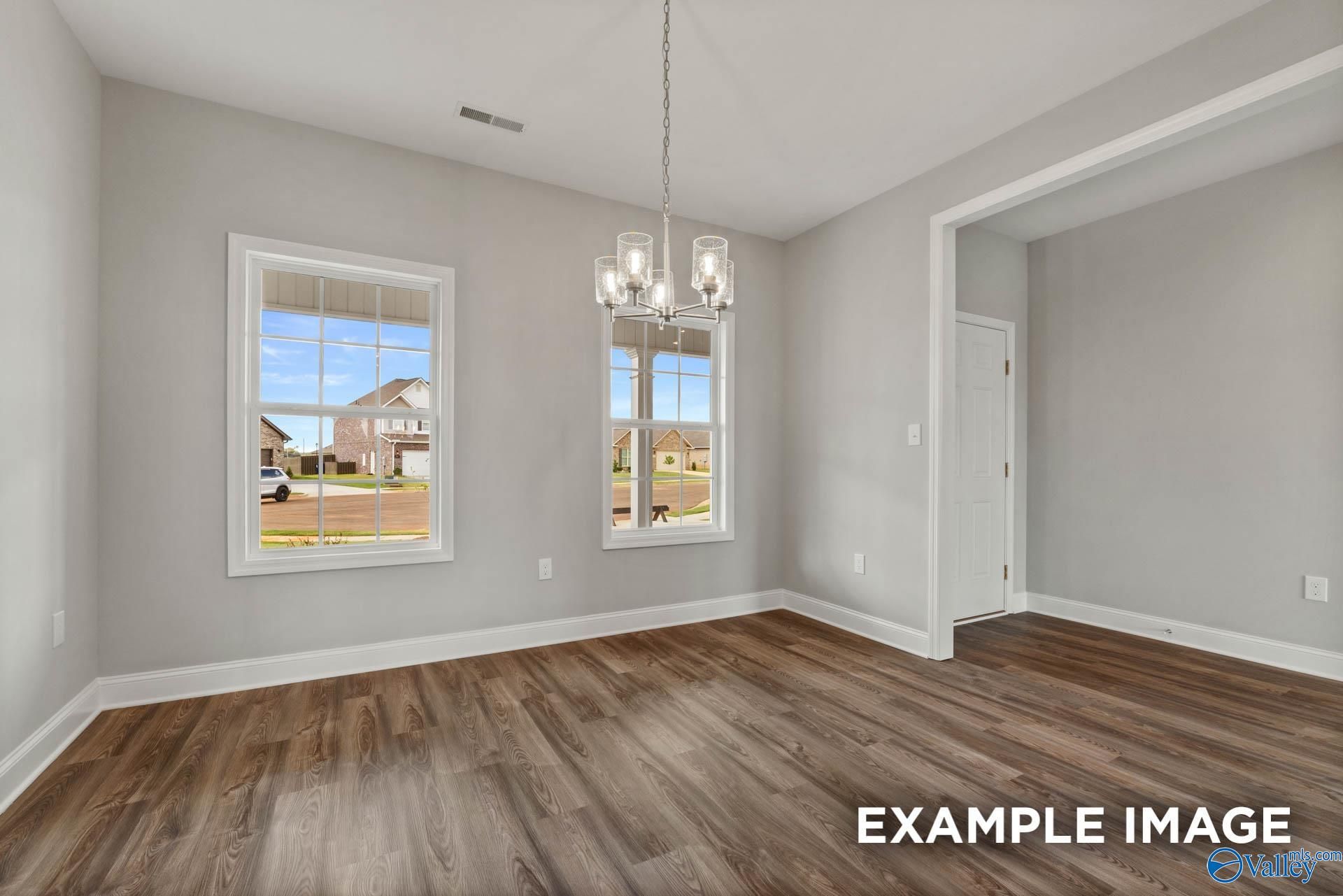 Spacious dining room with gray walls, large windows, modern chandelier, open archway, and hardwood floors in Davidson Homes The Shelby B, Athens Alabama