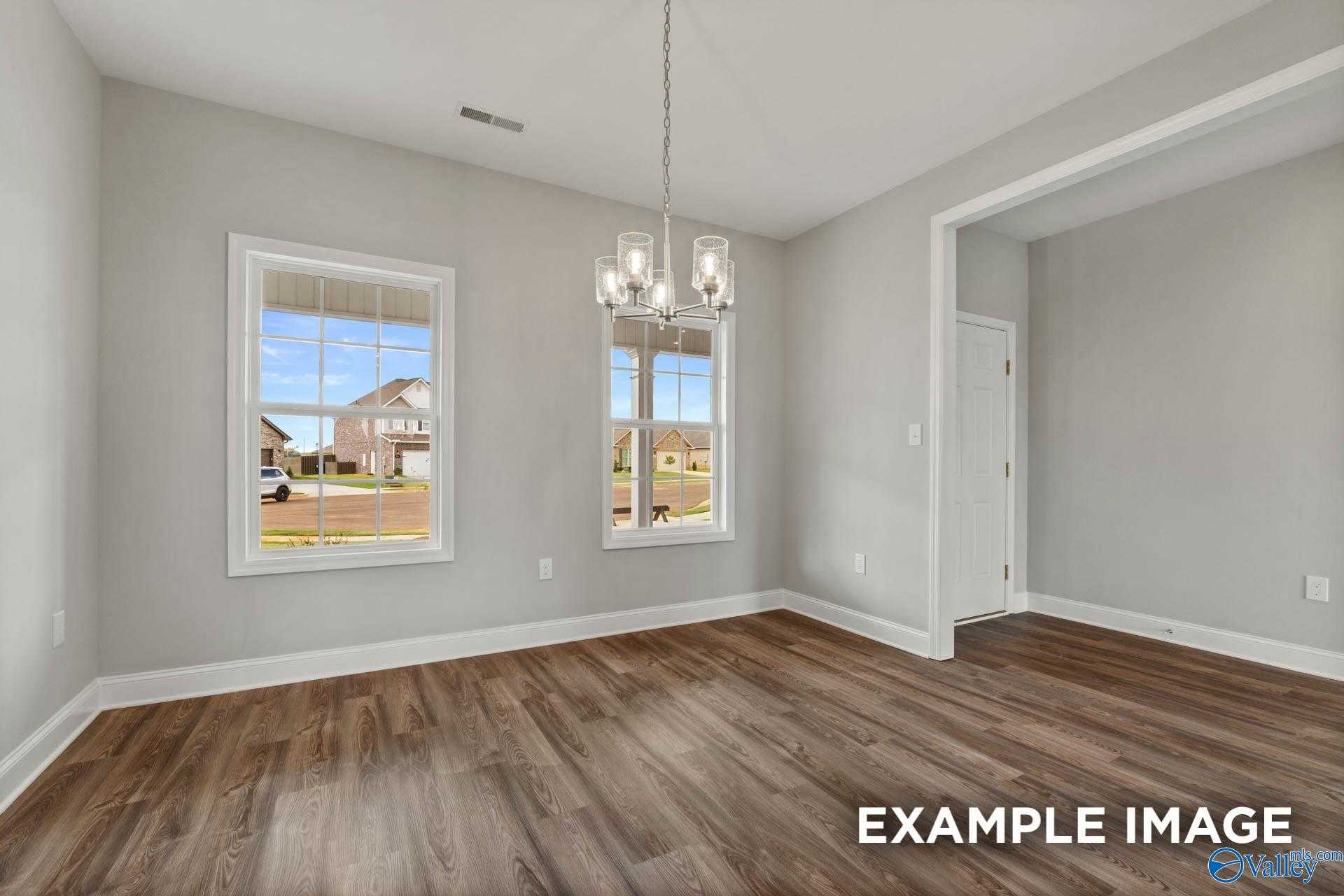 Spacious dining room with gray walls, large windows, modern chandelier, open archway, and hardwood floors in Davidson Homes The Shelby B, Athens Alabama