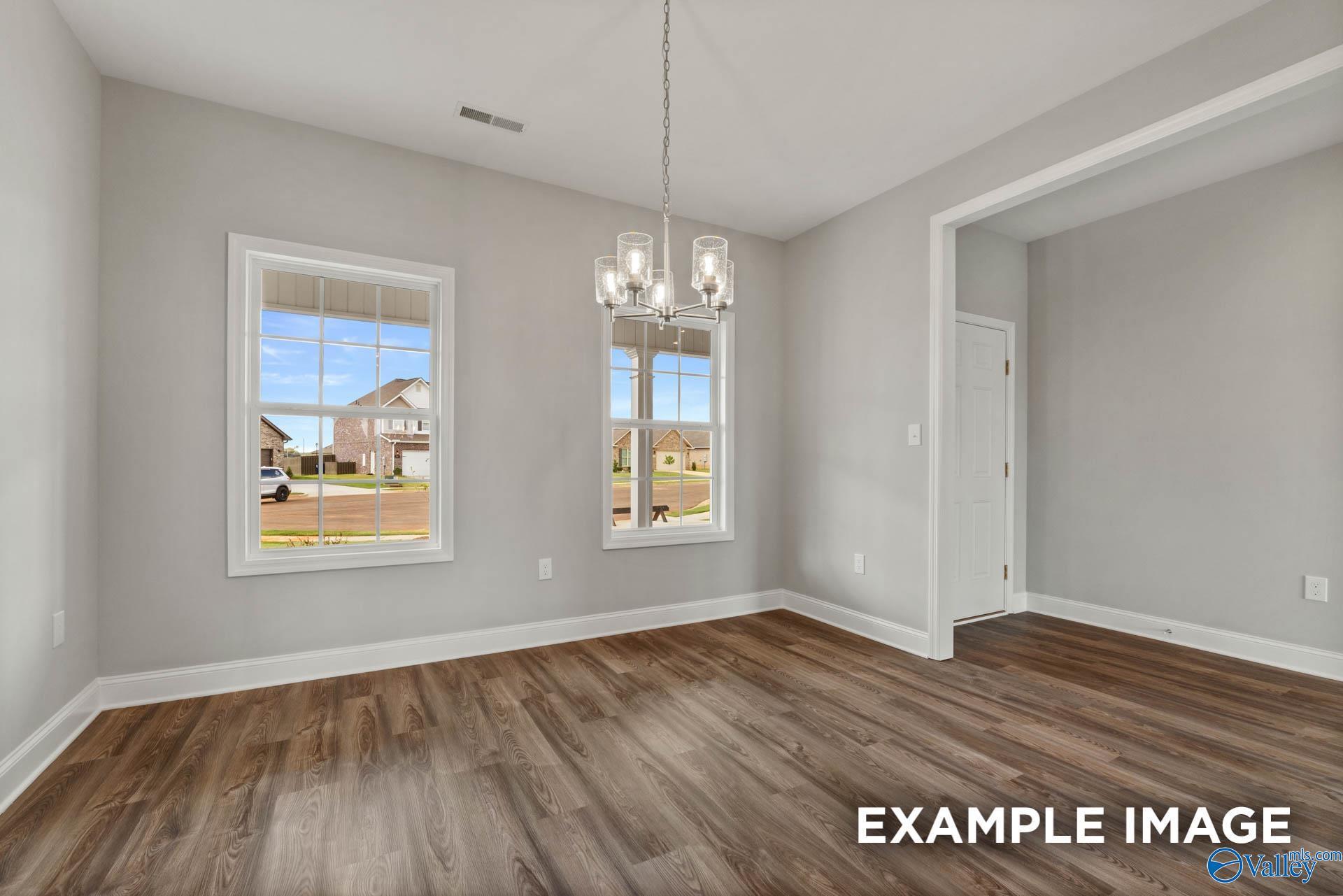 Spacious dining room with gray walls, large windows, modern chandelier, open archway, and hardwood floors in Davidson Homes The Shelby B, Athens Alabama