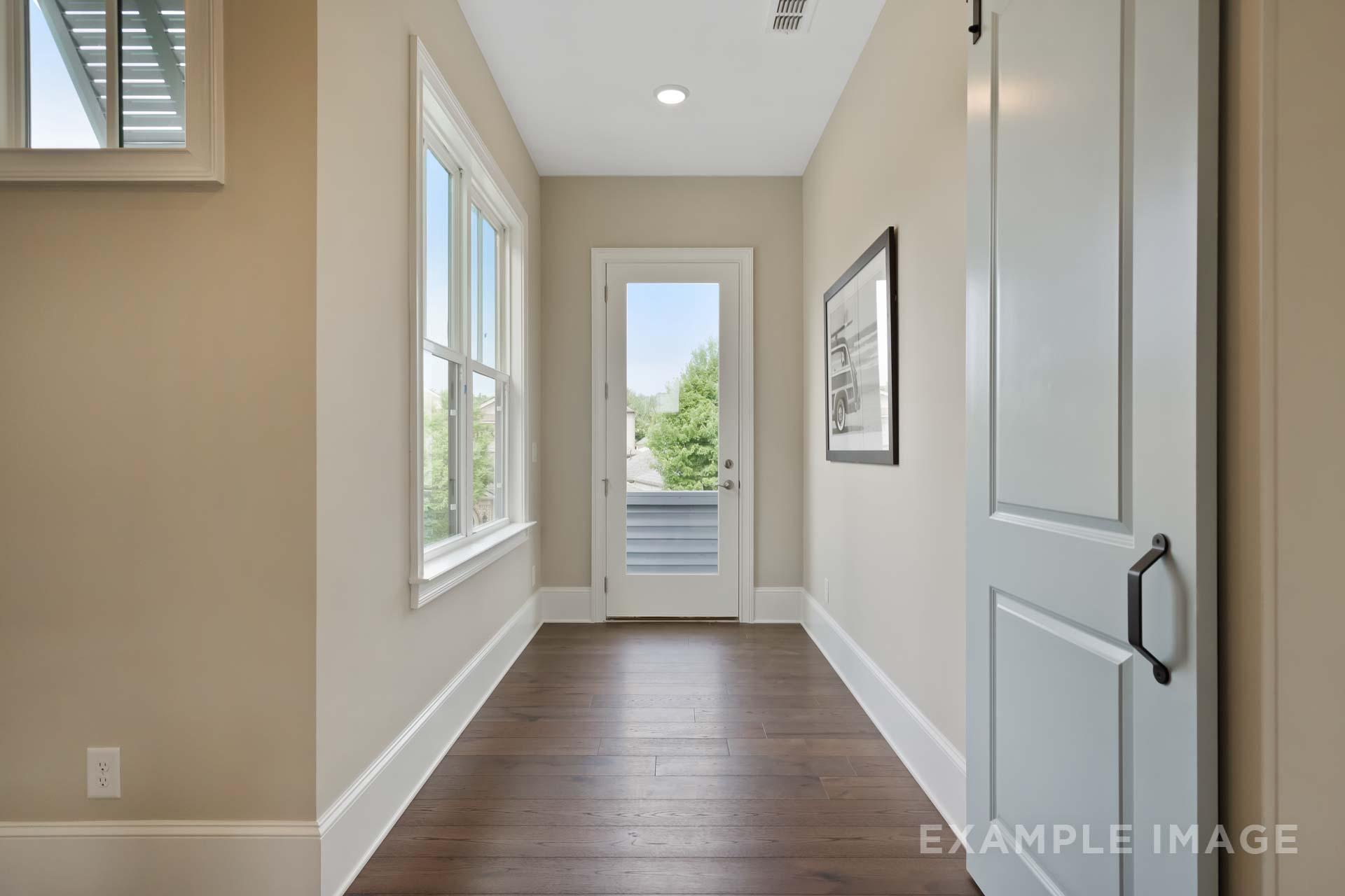 Spacious upstairs hallway in The Seaside C home with beige walls, hardwood floors, large windows, and French doors to deck