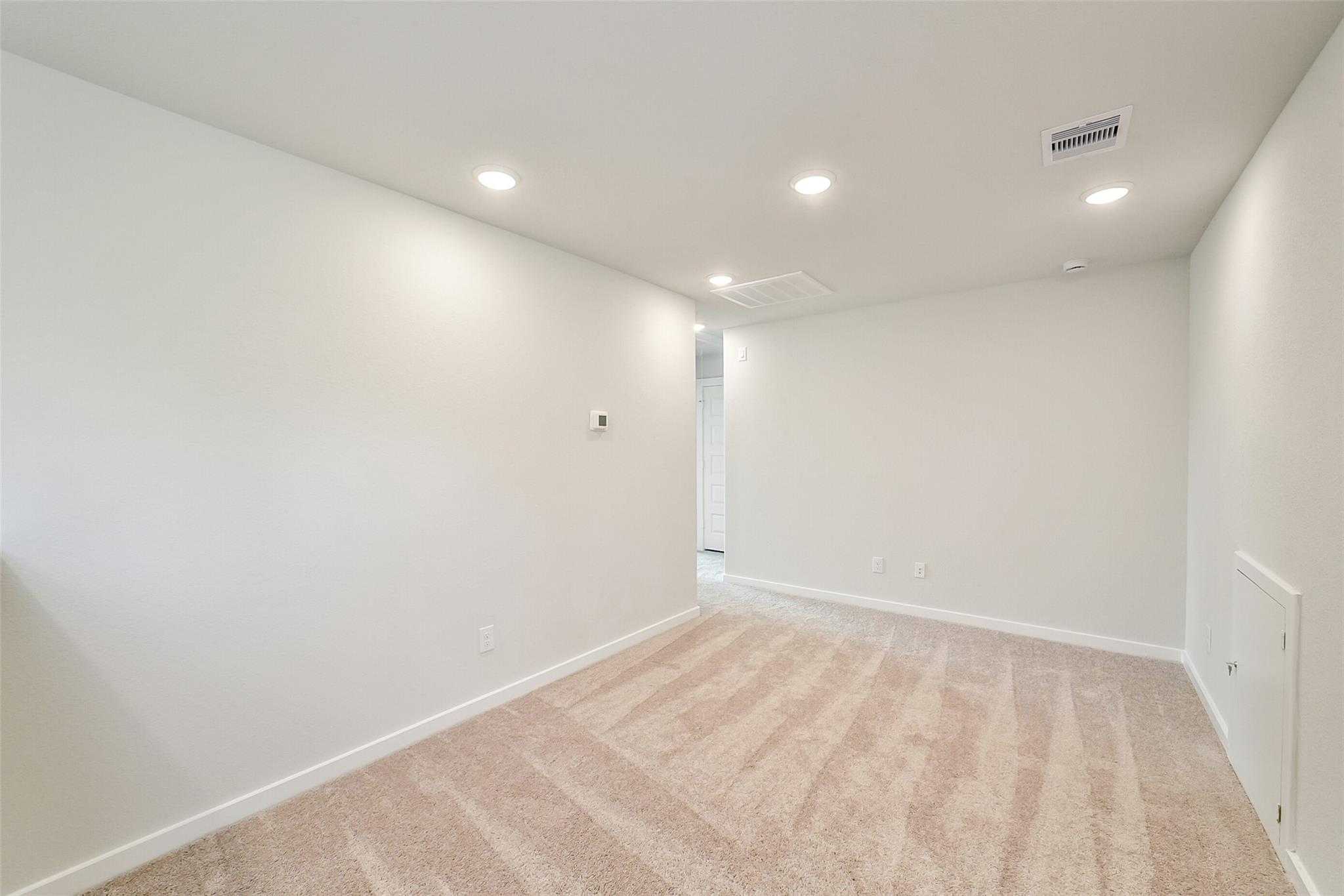 Spacious empty bedroom with white walls, beige carpet, recessed lights in Davidson Homes The Blanco E, Magnolia, Texas