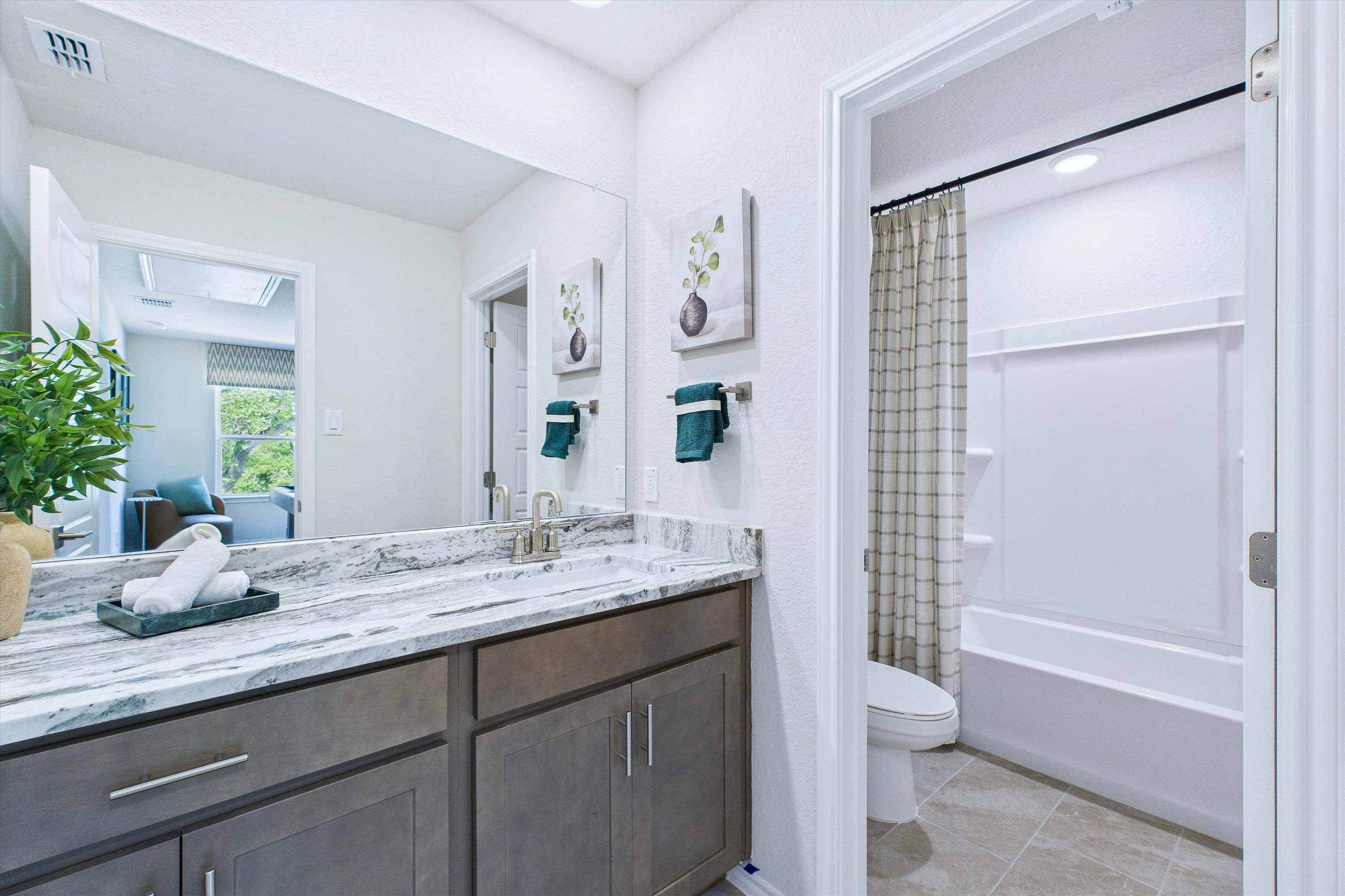 Modern bathroom in The Gillian C featuring a marble vanity top, dark wood cabinetry, and a clean shower-tub combo.