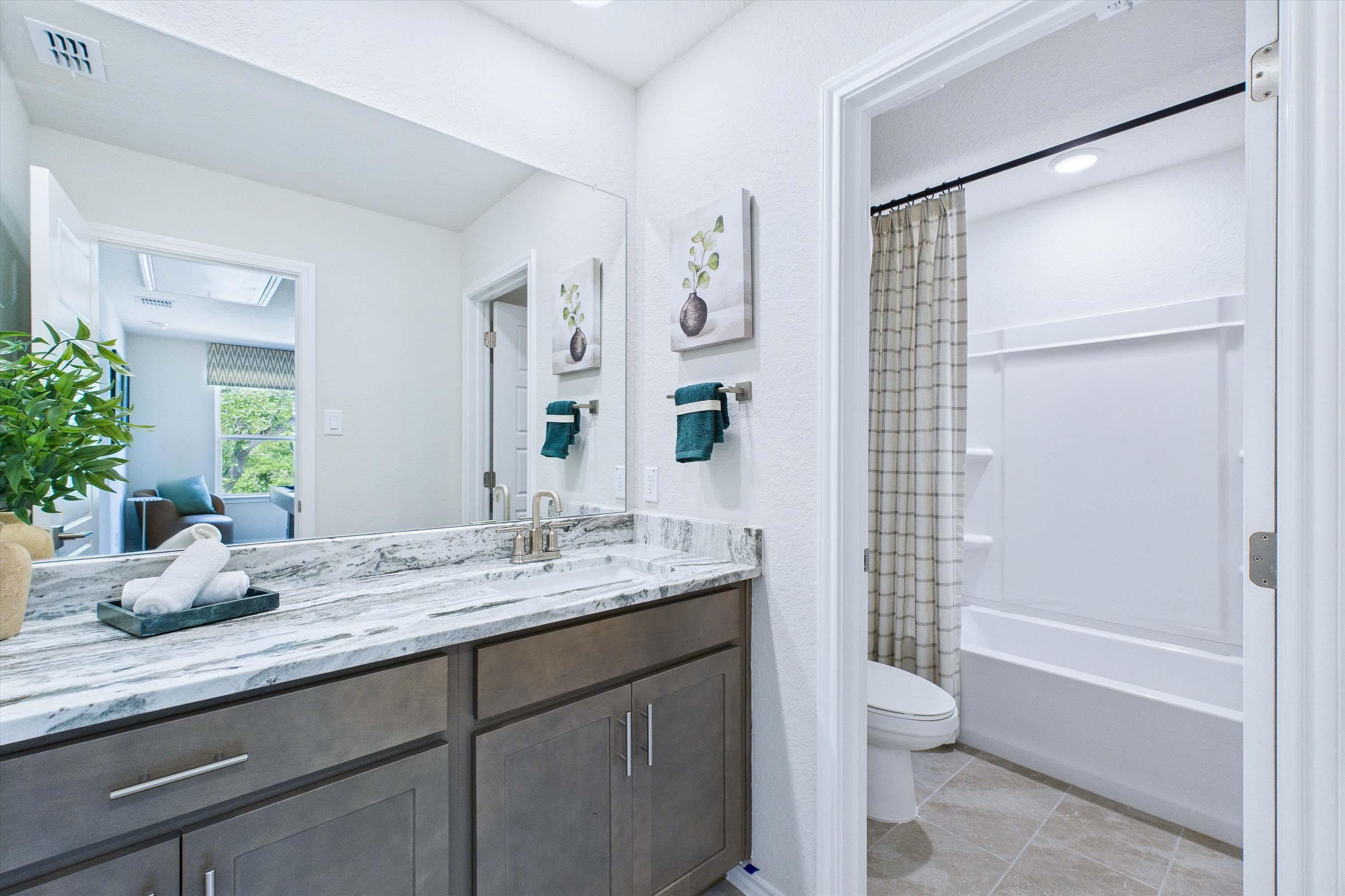 Modern bathroom in The Gillian C featuring a marble vanity top, dark wood cabinetry, and a clean shower-tub combo.