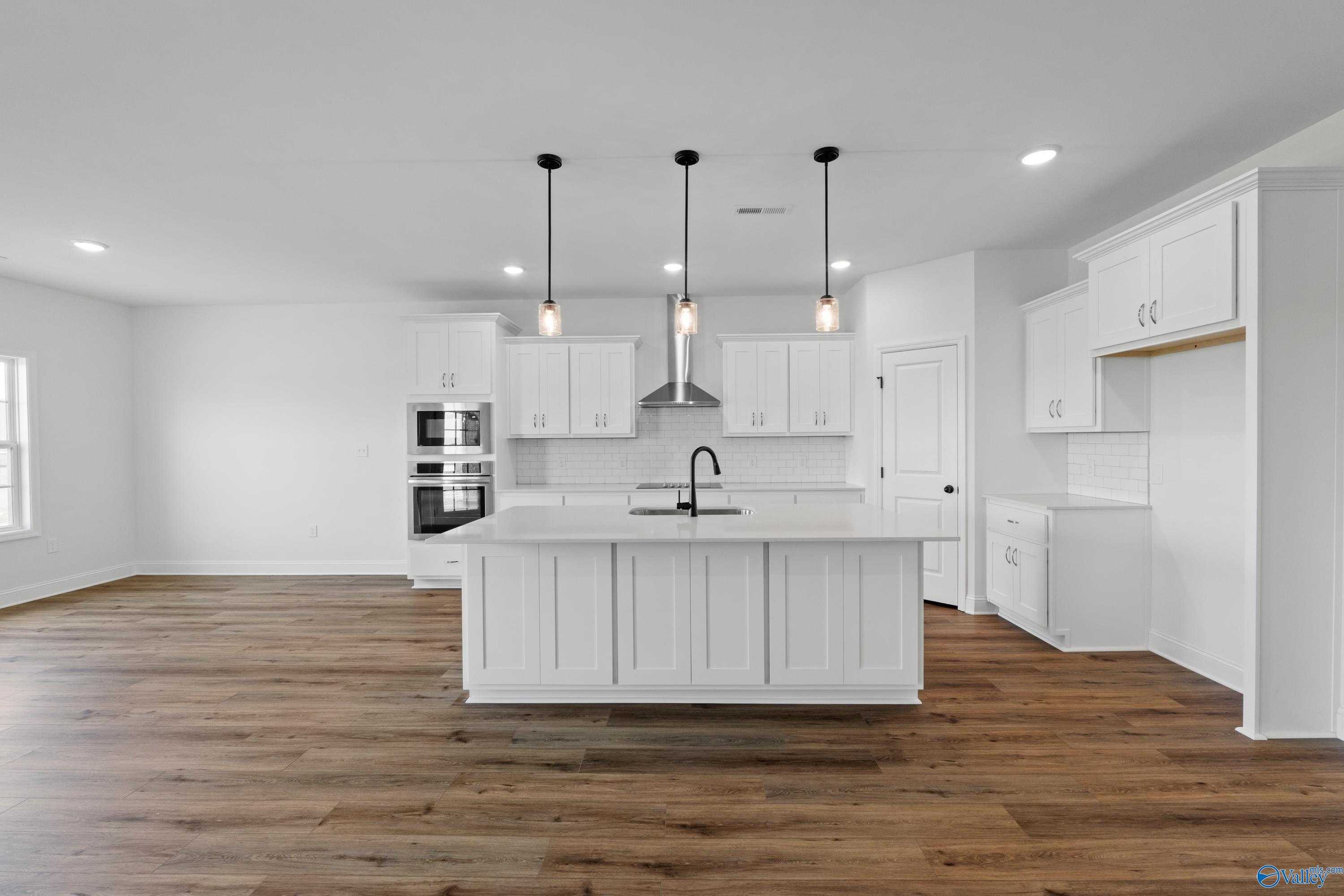 Modern white kitchen featuring large center island, pendant lights, stainless sink, and hardwood floors in The Rockford B, Toney, Alabama