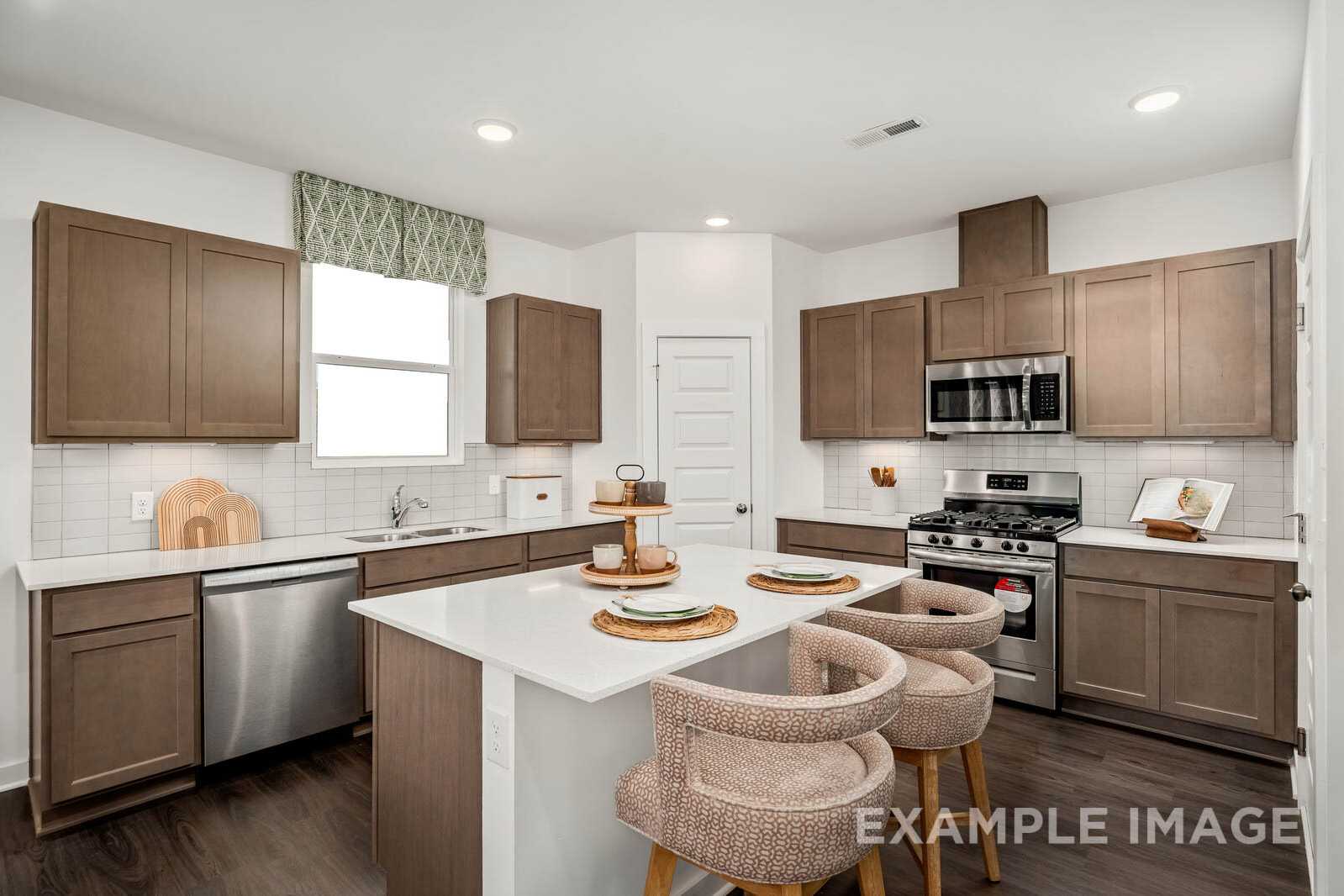 Spacious kitchen in The Gordon B showcasing shaker wood cabinets, white quartz island with bar stools, and stainless steel appliances