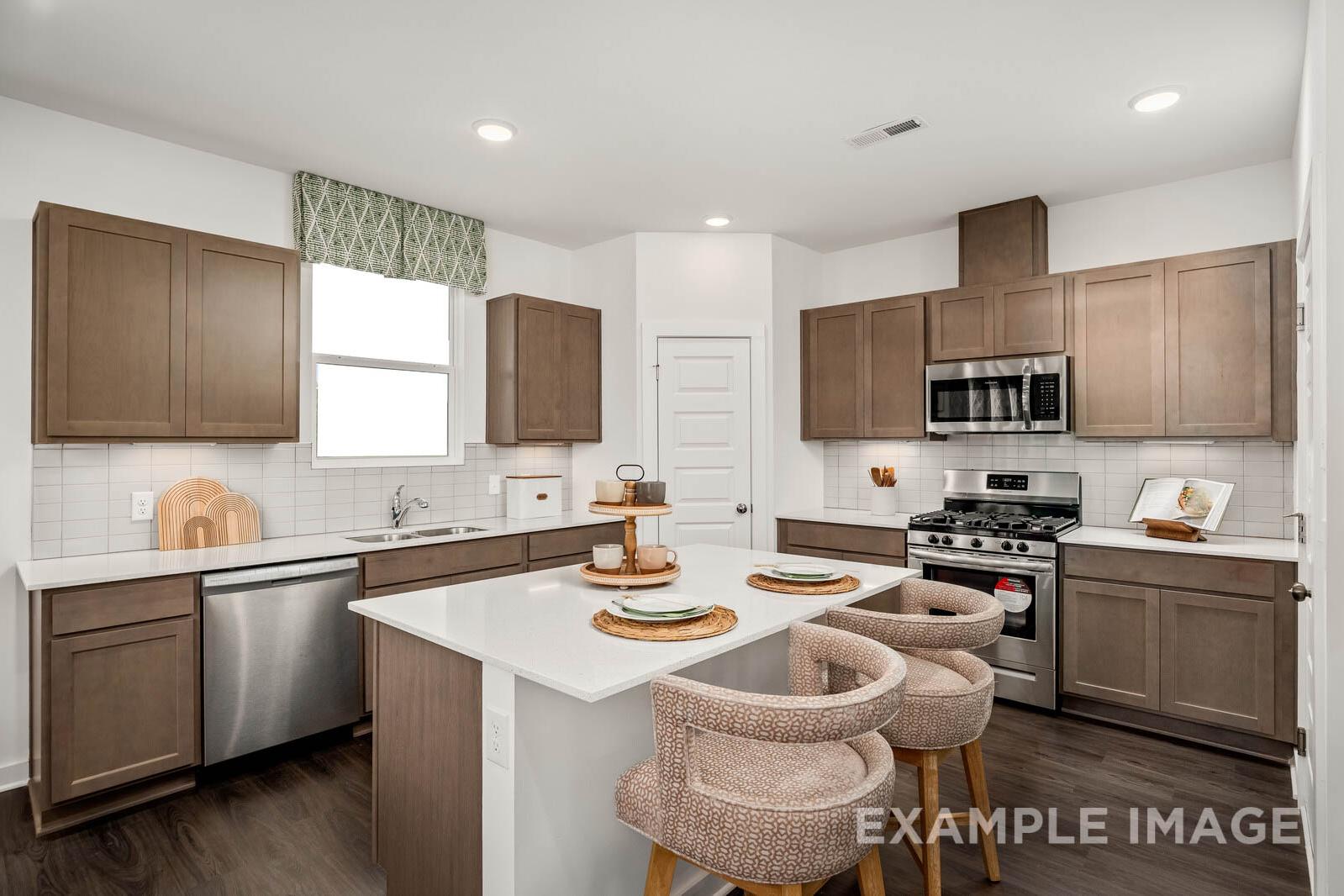 Spacious kitchen in The Gordon C featuring light shaker cabinets, white quartz island, stainless steel appliances