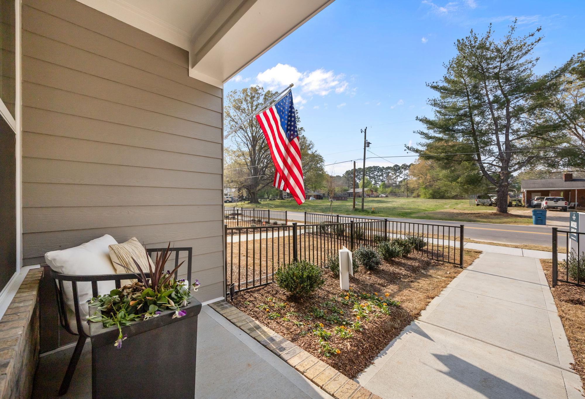 Front porch view of The Mitchell in Knightdale, NC featuring cozy seating, landscaping, and an American flag.