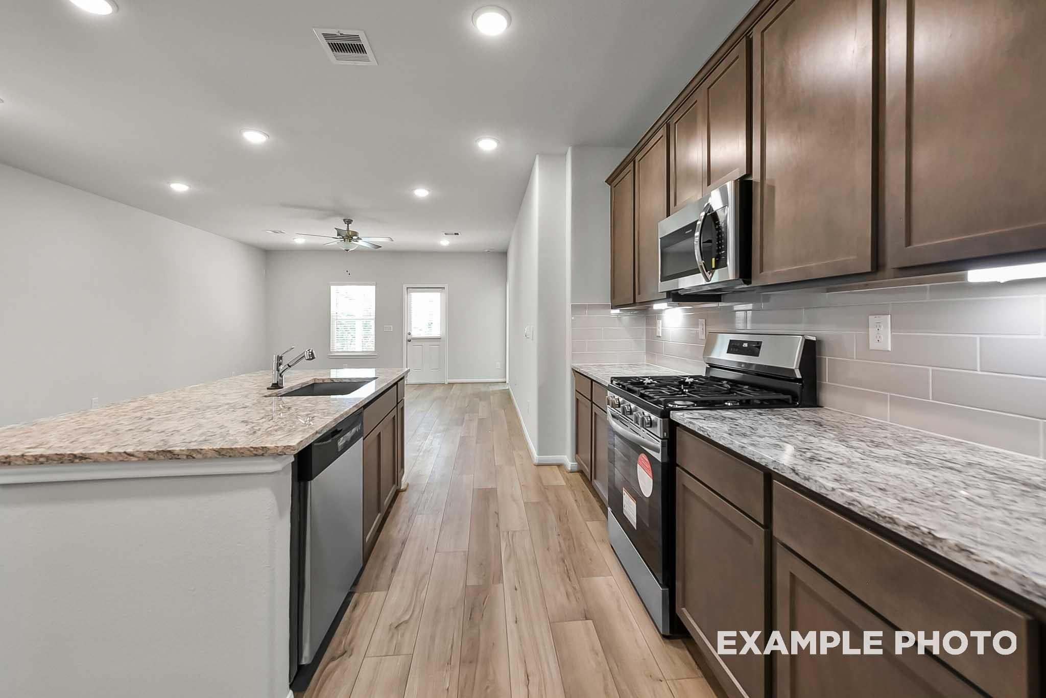 Modern kitchen with granite countertops, stainless appliances, and wood-style flooring in The Blanco F, Spring Branch Crossing.