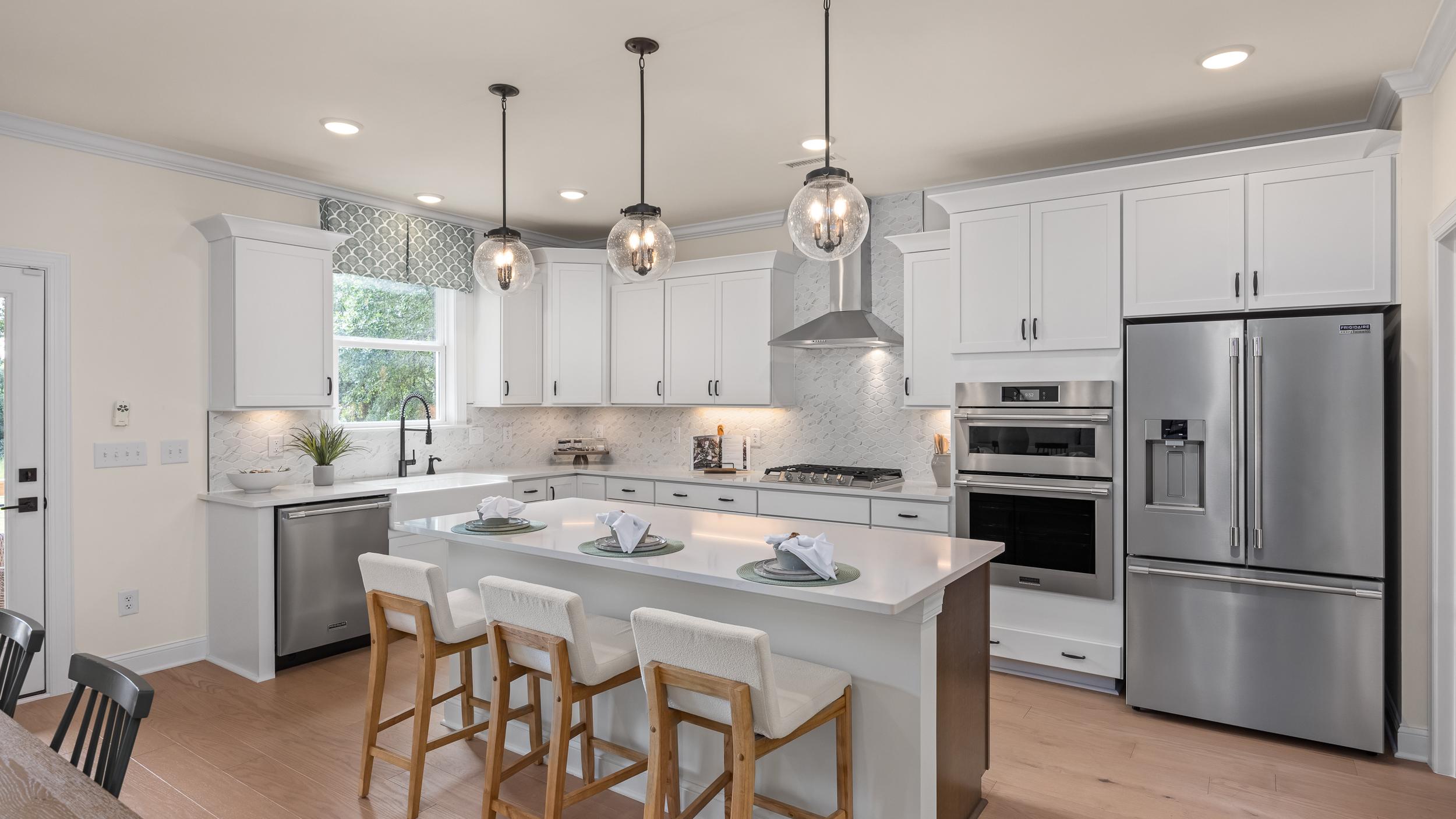 Modern kitchen at Laneridge Estates in Raleigh NC with white shaker cabinets, large island, stainless steel appliances, pendant lights, hardwood floors