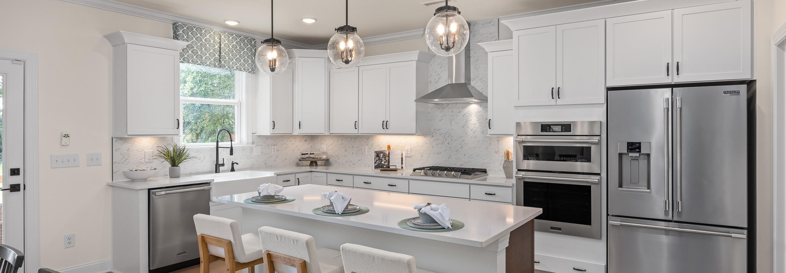 Modern kitchen at Laneridge Estates in Raleigh NC with white shaker cabinets, large island, stainless steel appliances, pendant lights, hardwood floors