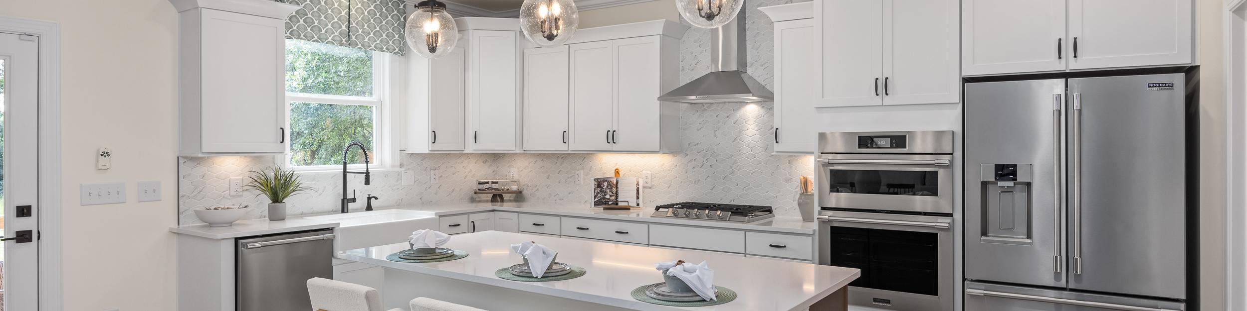 Modern kitchen at Laneridge Estates in Raleigh NC with white shaker cabinets, large island, stainless steel appliances, pendant lights, hardwood floors
