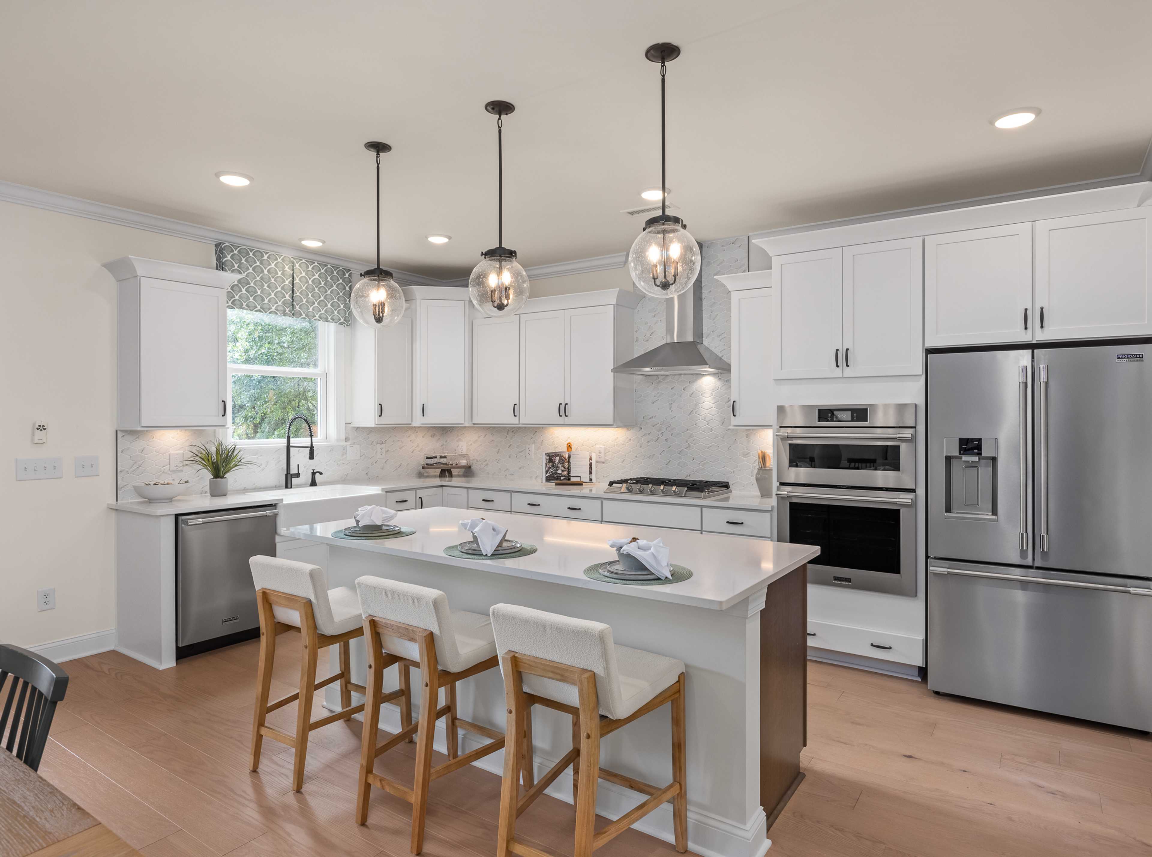 Modern kitchen at Laneridge Estates in Raleigh NC with white shaker cabinets, large island, stainless steel appliances, pendant lights, hardwood floors
