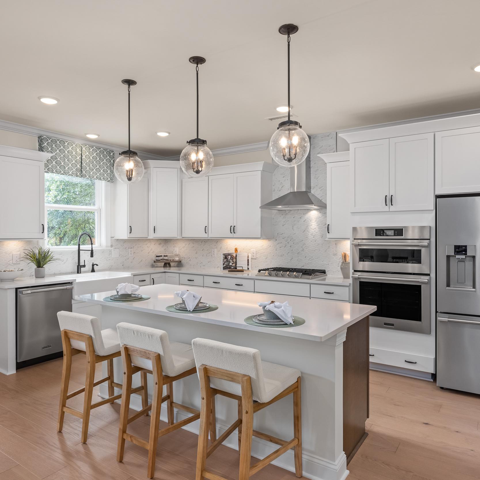 Modern kitchen at Laneridge Estates in Raleigh NC with white shaker cabinets, large island, stainless steel appliances, pendant lights, hardwood floors