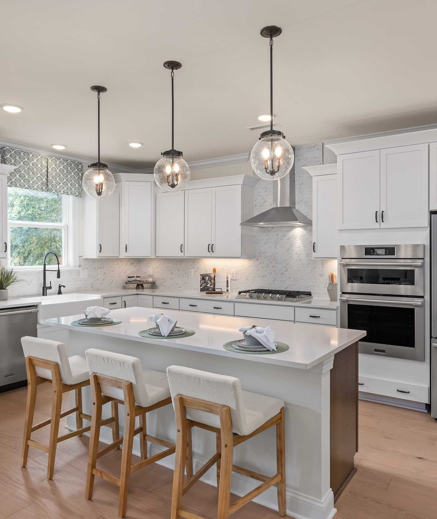 Modern kitchen at Laneridge Estates in Raleigh NC with white shaker cabinets, large island, stainless steel appliances, pendant lights, hardwood floors