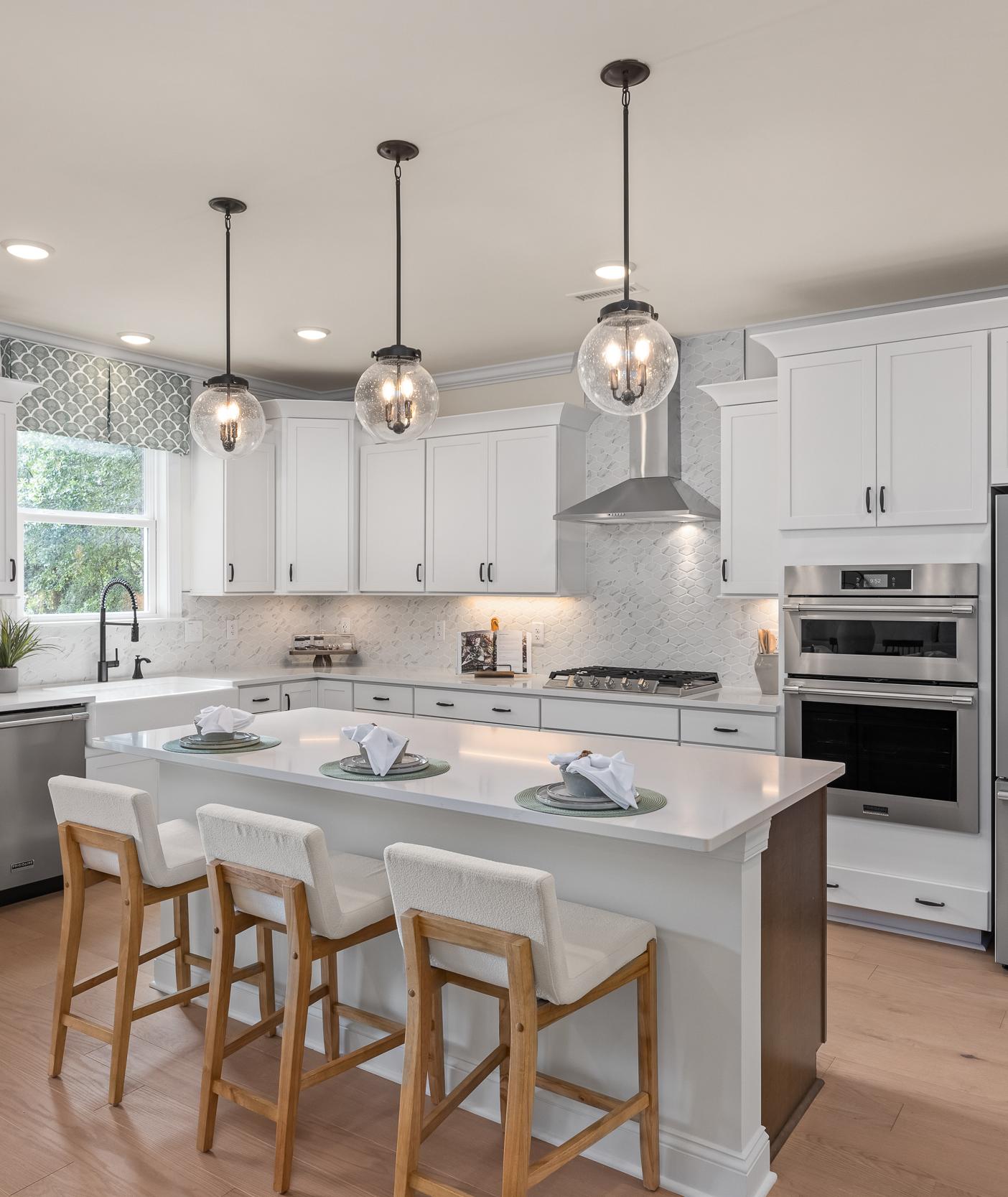 Modern kitchen at Laneridge Estates in Raleigh NC with white shaker cabinets, large island, stainless steel appliances, pendant lights, hardwood floors