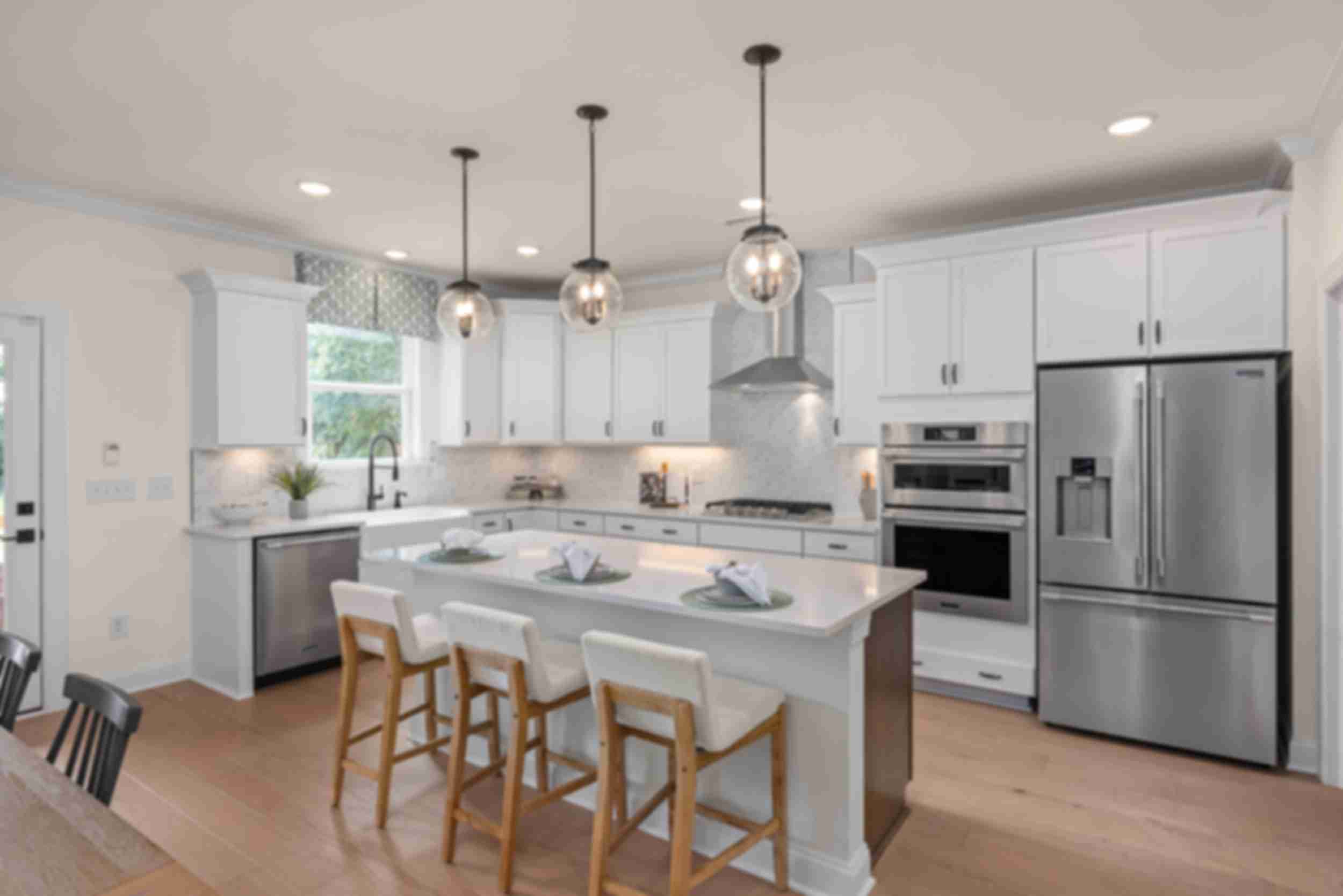 Modern kitchen at Laneridge Estates in Raleigh NC with white shaker cabinets, large island, stainless steel appliances, pendant lights, hardwood floors