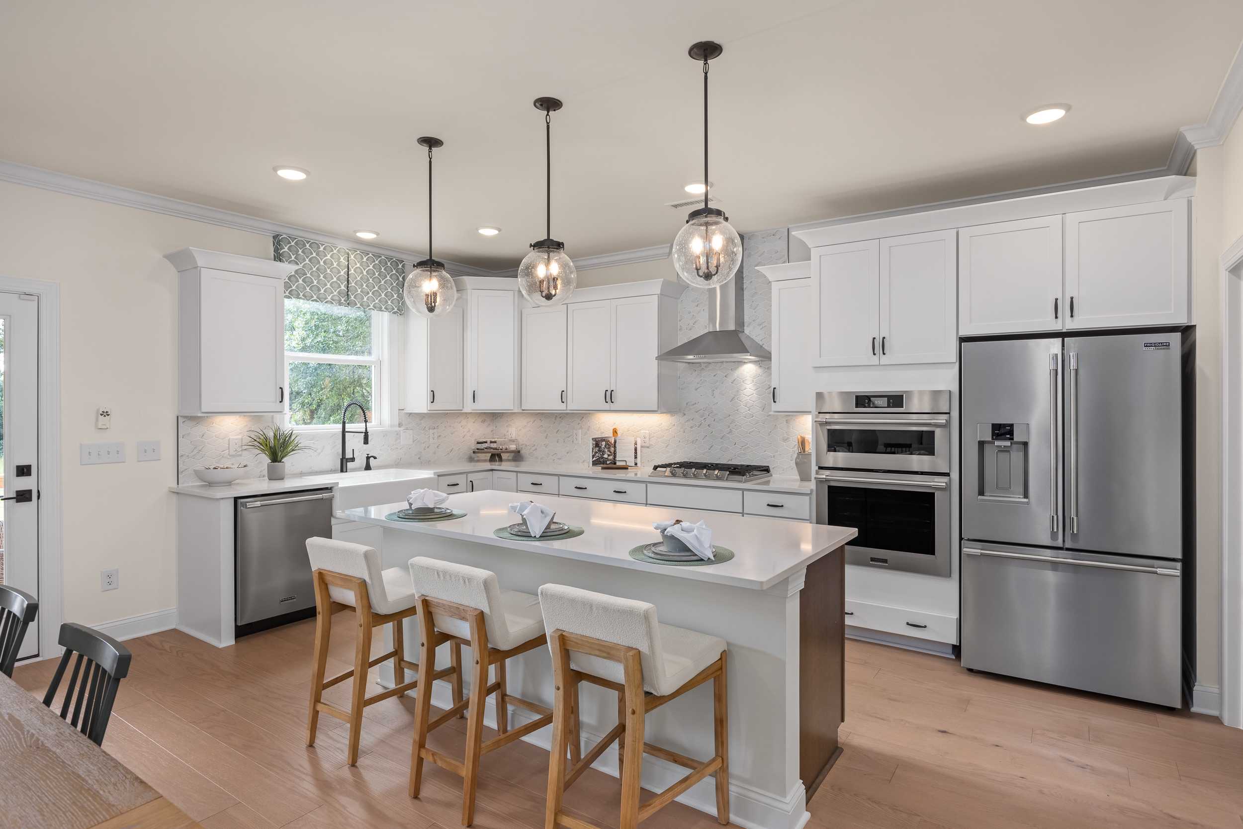 Modern kitchen at Laneridge Estates in Raleigh NC with white shaker cabinets, large island, stainless steel appliances, pendant lights, hardwood floors