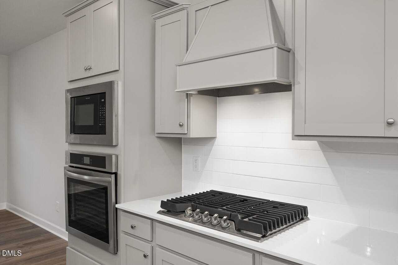 Modern white kitchen featuring stainless steel double oven and gas cooktop in Davidson Homes The Warren, Fuquay-Varina, NC