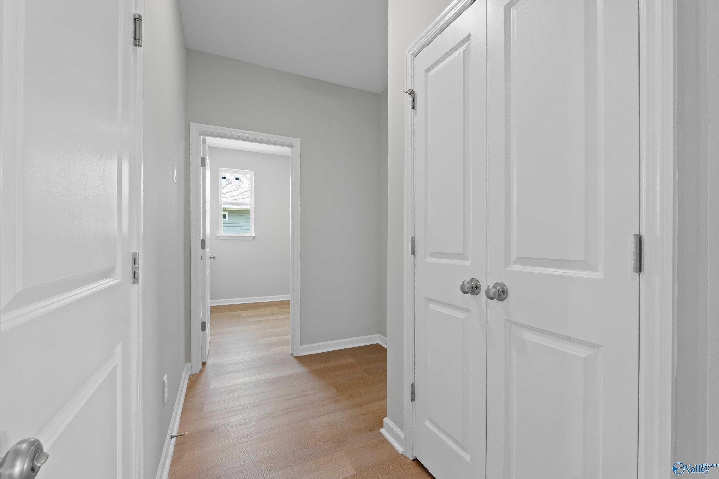 Bright hallway with white doors, gray walls, and hardwood floors in The Aurora 4-bedroom home, Harvest, Alabama